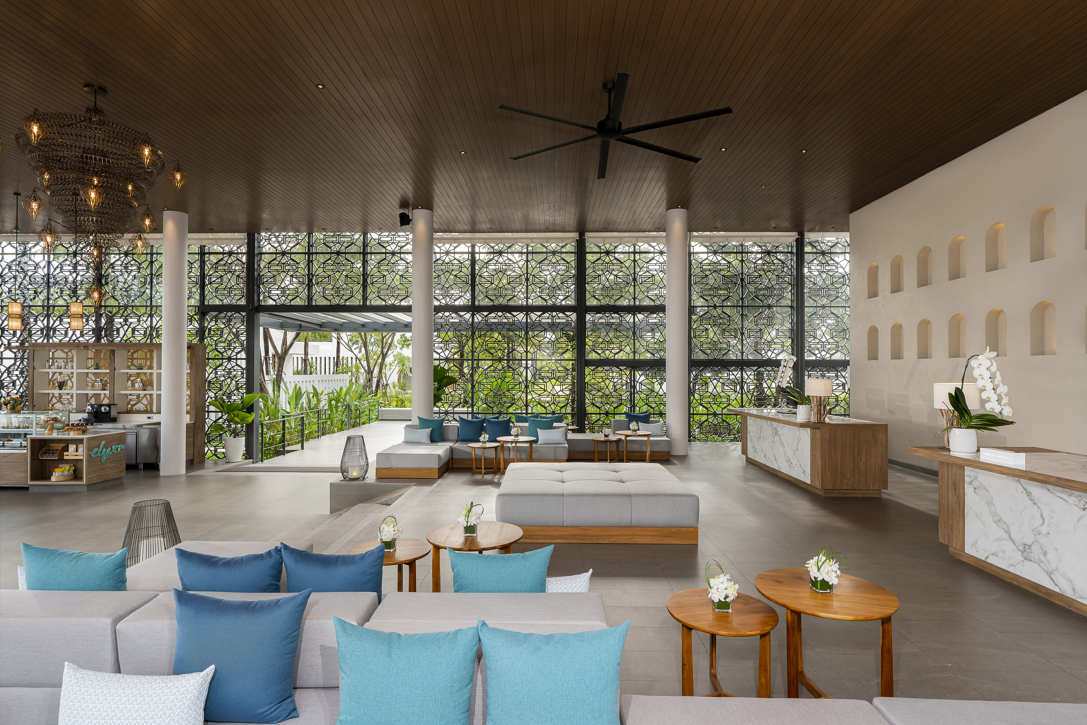 Stylish tropical hotel lounge with blue sofas, wooden tables, and patterned windows.