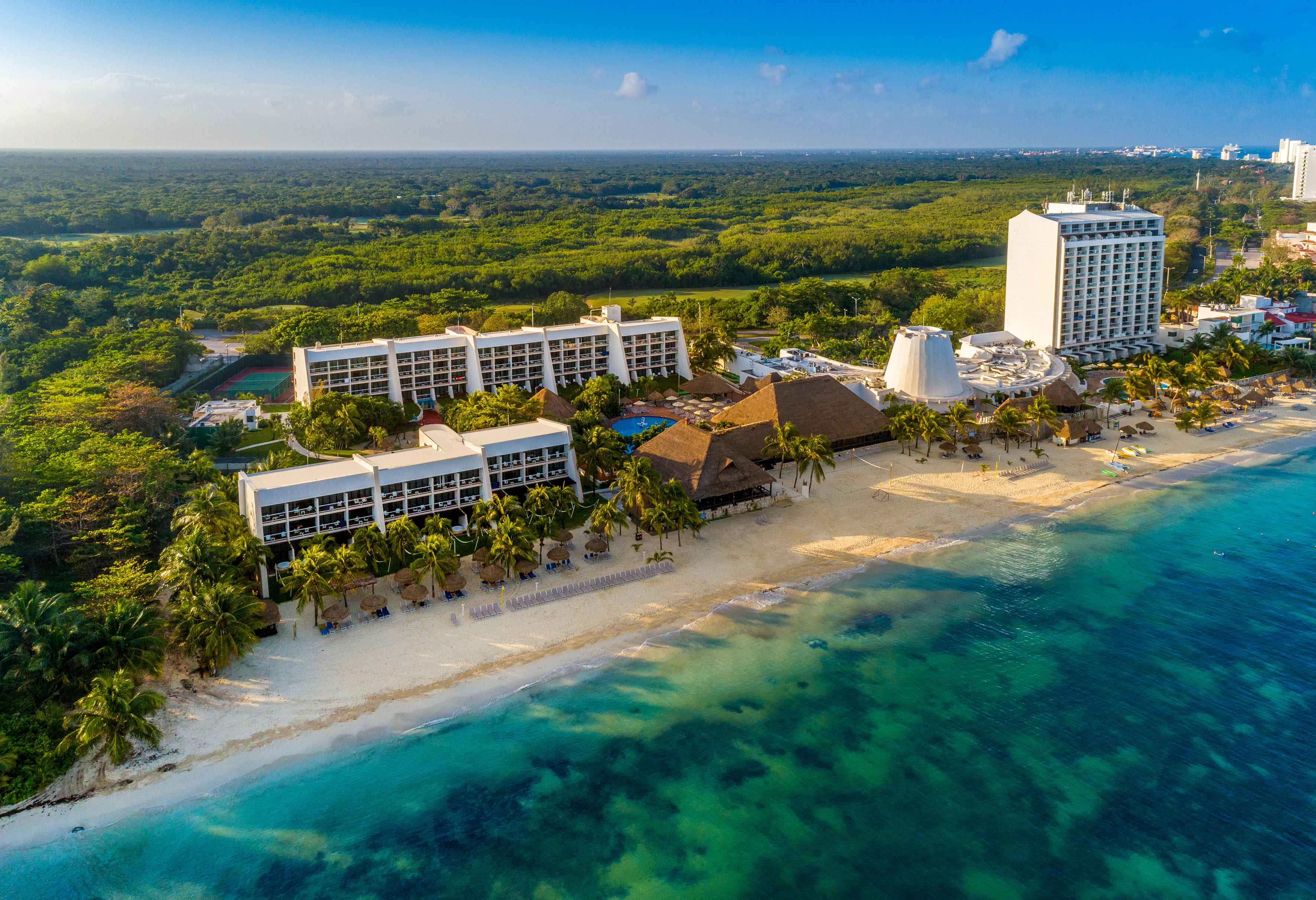 Resort tropical en playa de arena blanca, mar turquesa, palmeras y selva.