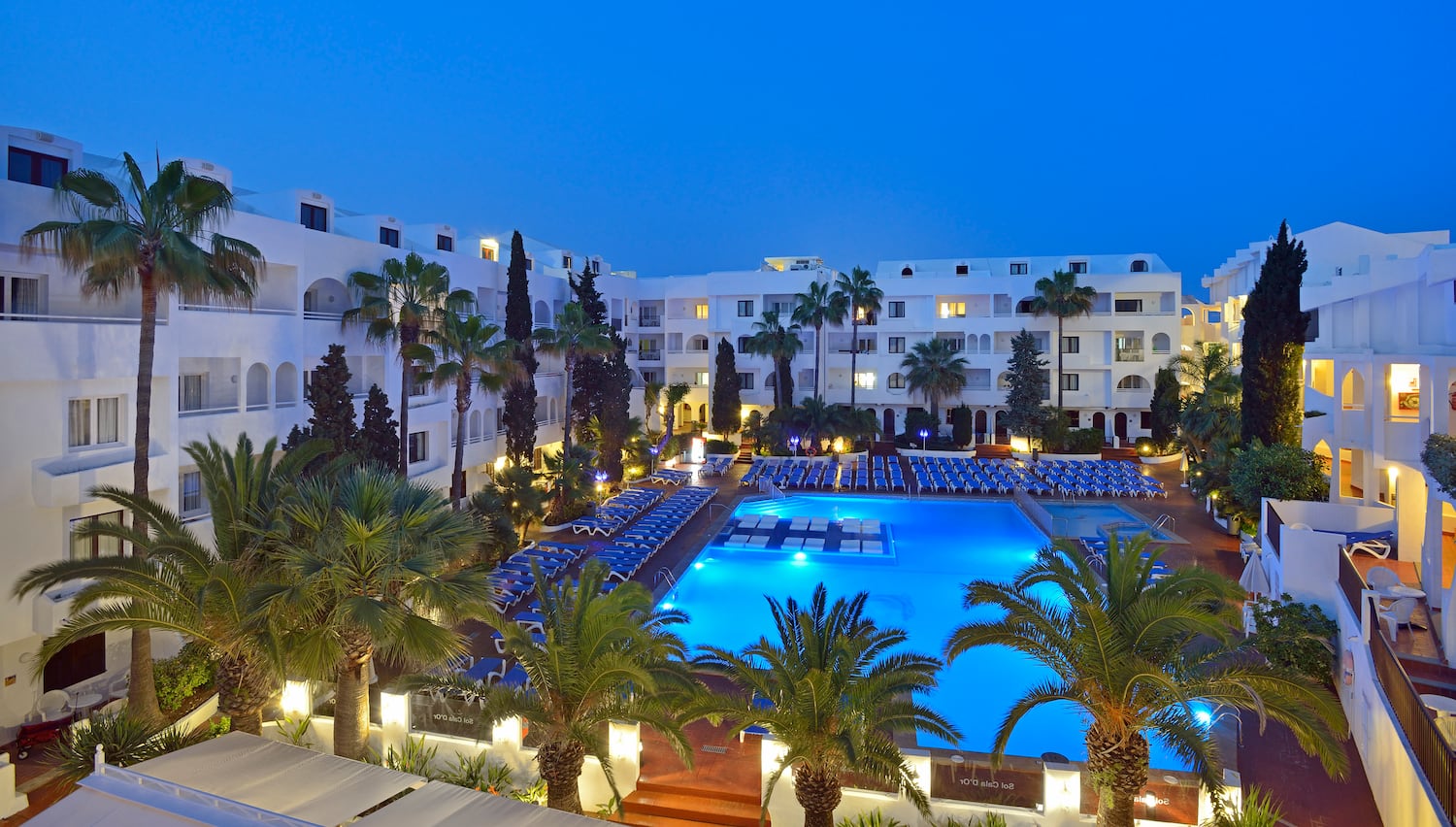 a pool and palm trees in front of a hotel