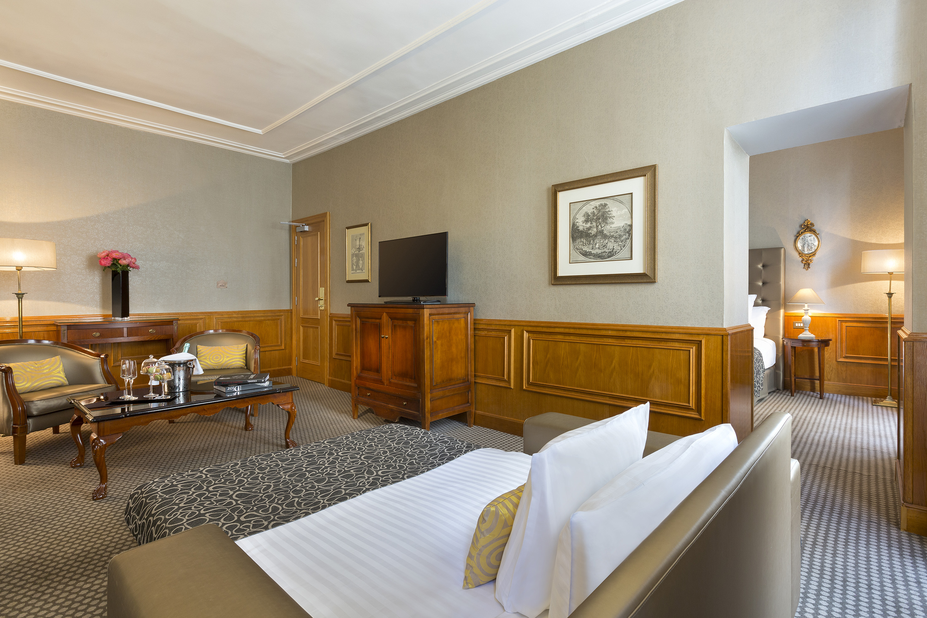 Elegant hotel suite with living area, wood paneling, and bedroom access.