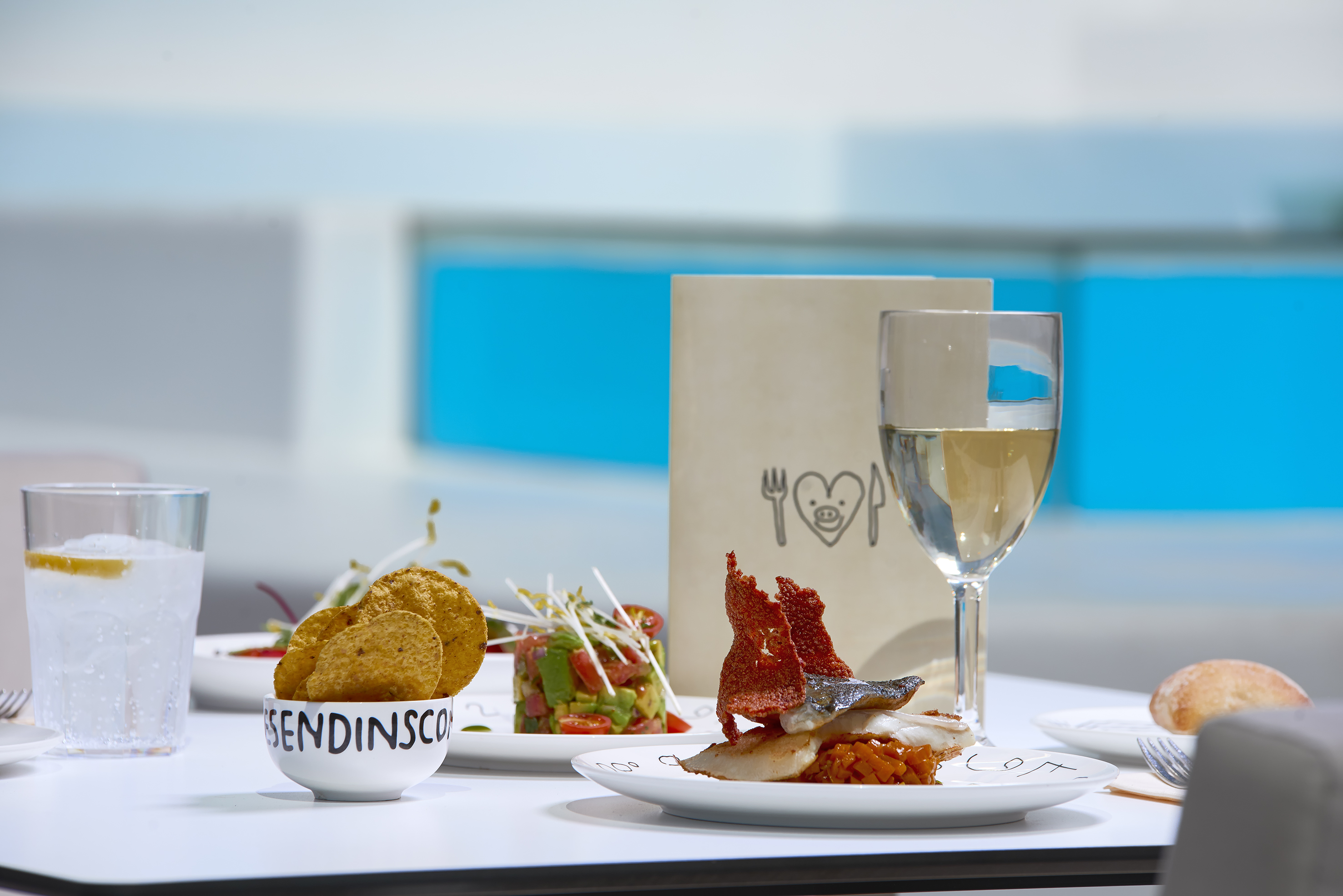 Gourmet fish meal, avocado salad, chips, white wine, and sparkling water.