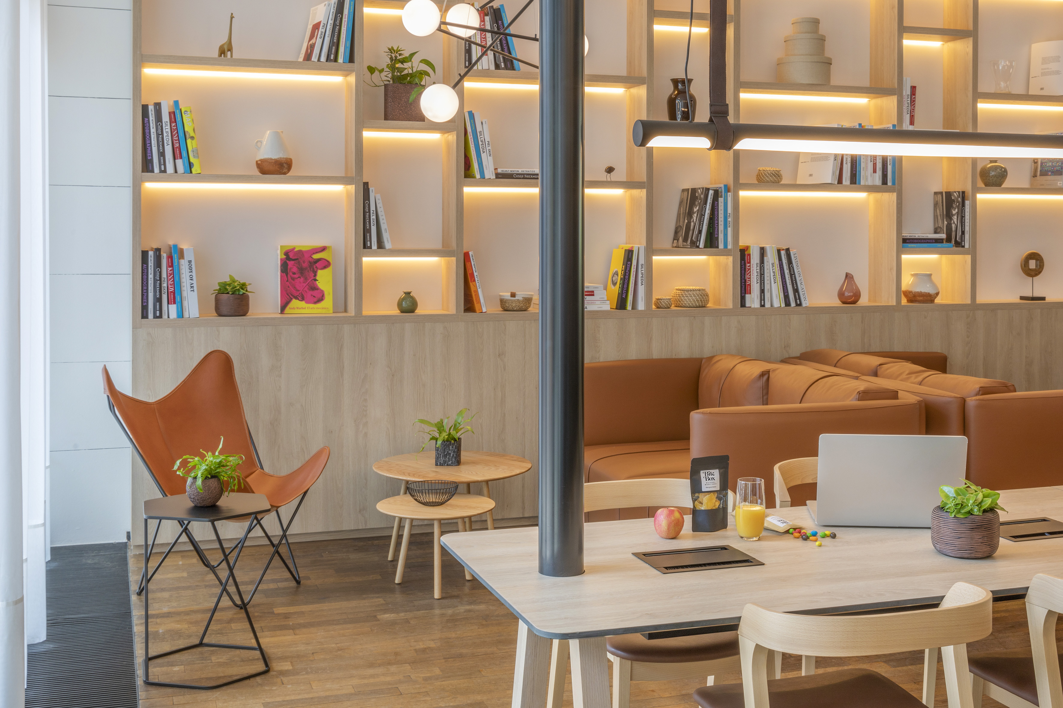 Stylish lounge with lighted bookshelves, tan sofa, and modern co-working table.