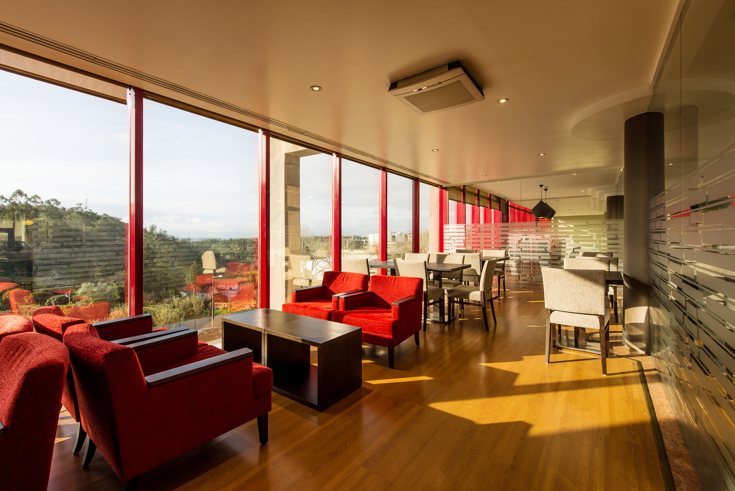 Modern cafe lounge with red armchairs, large windows, scenic view, wooden floor.