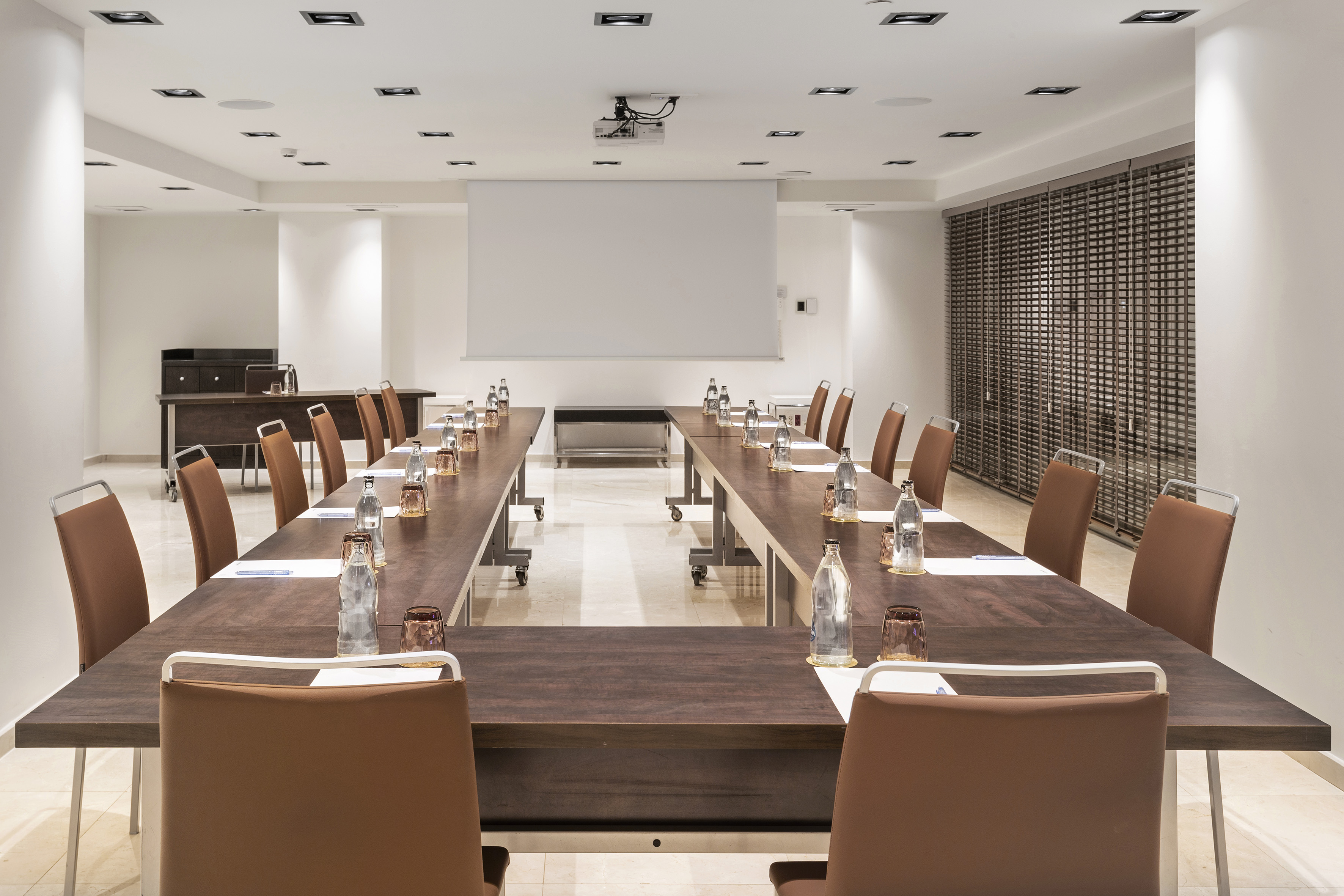Modern U-shaped conference room with brown chairs, projector, and screen.