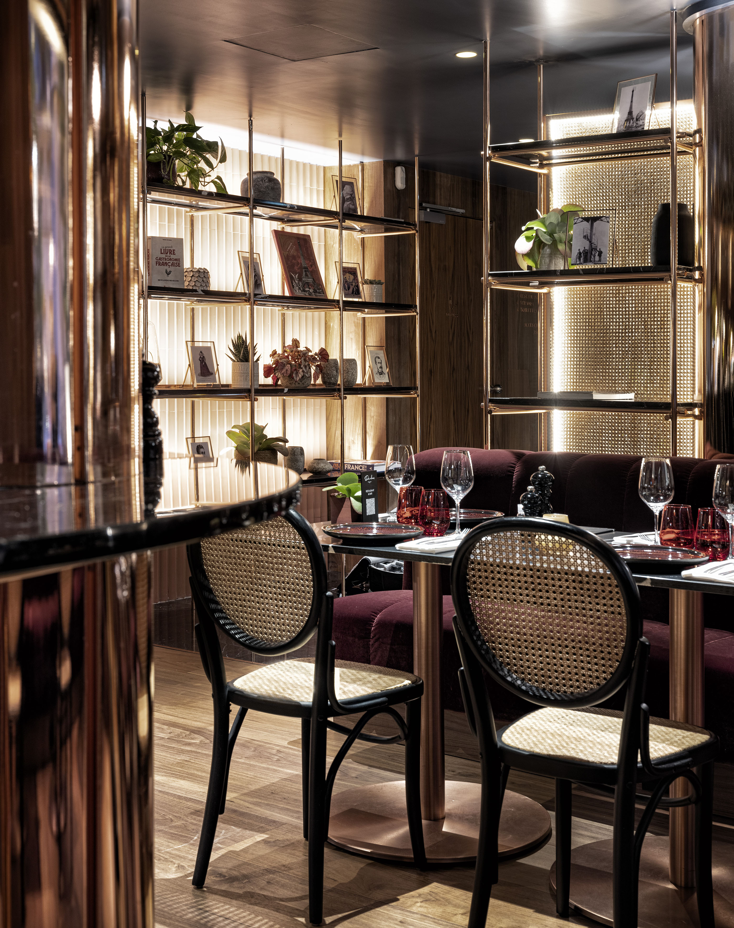 Chic restaurant interior: dark velvet, gold illuminated shelves, and cane chairs.
