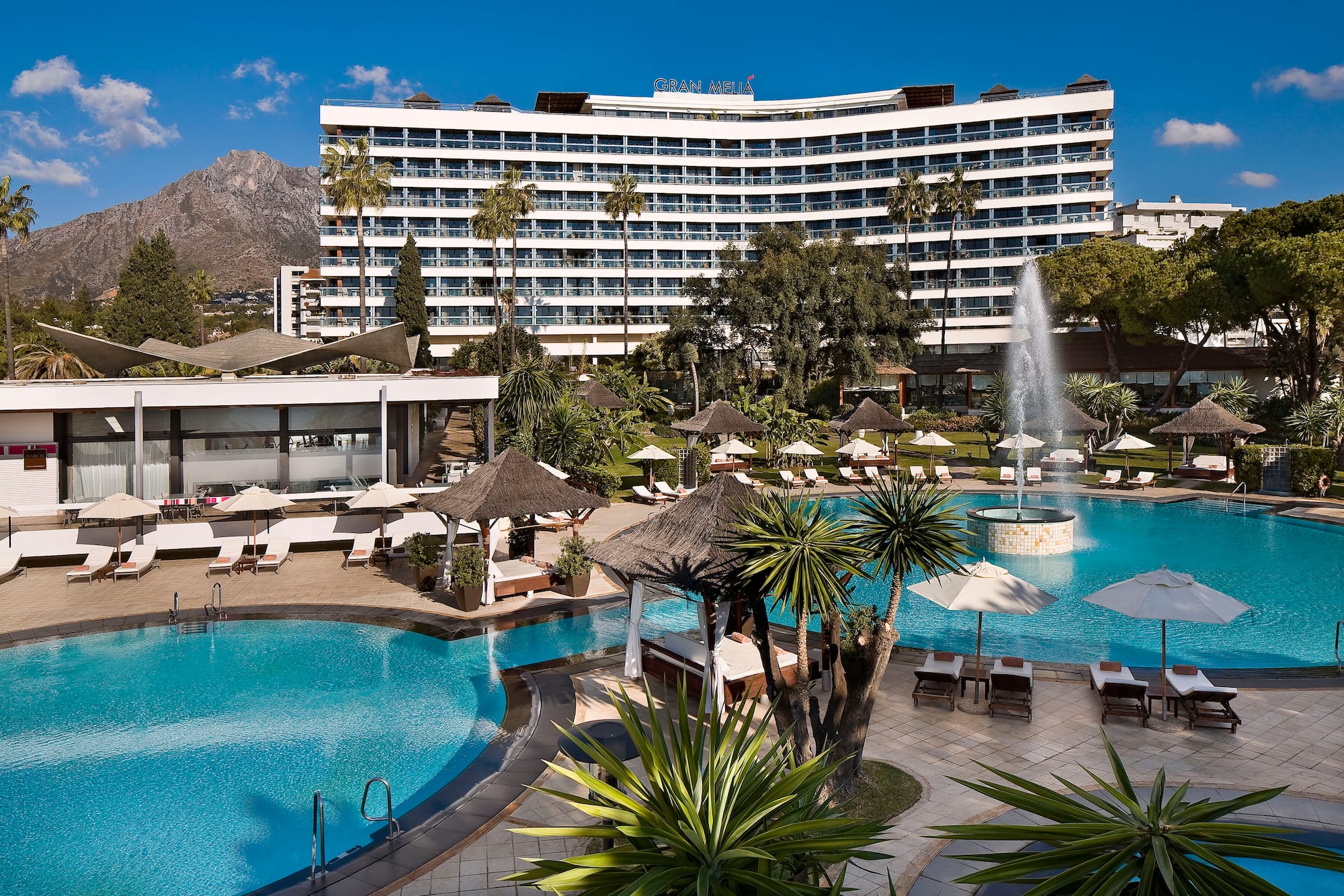 Gran Melia resort pool, sun loungers, fountain, palm trees, and mountain view.