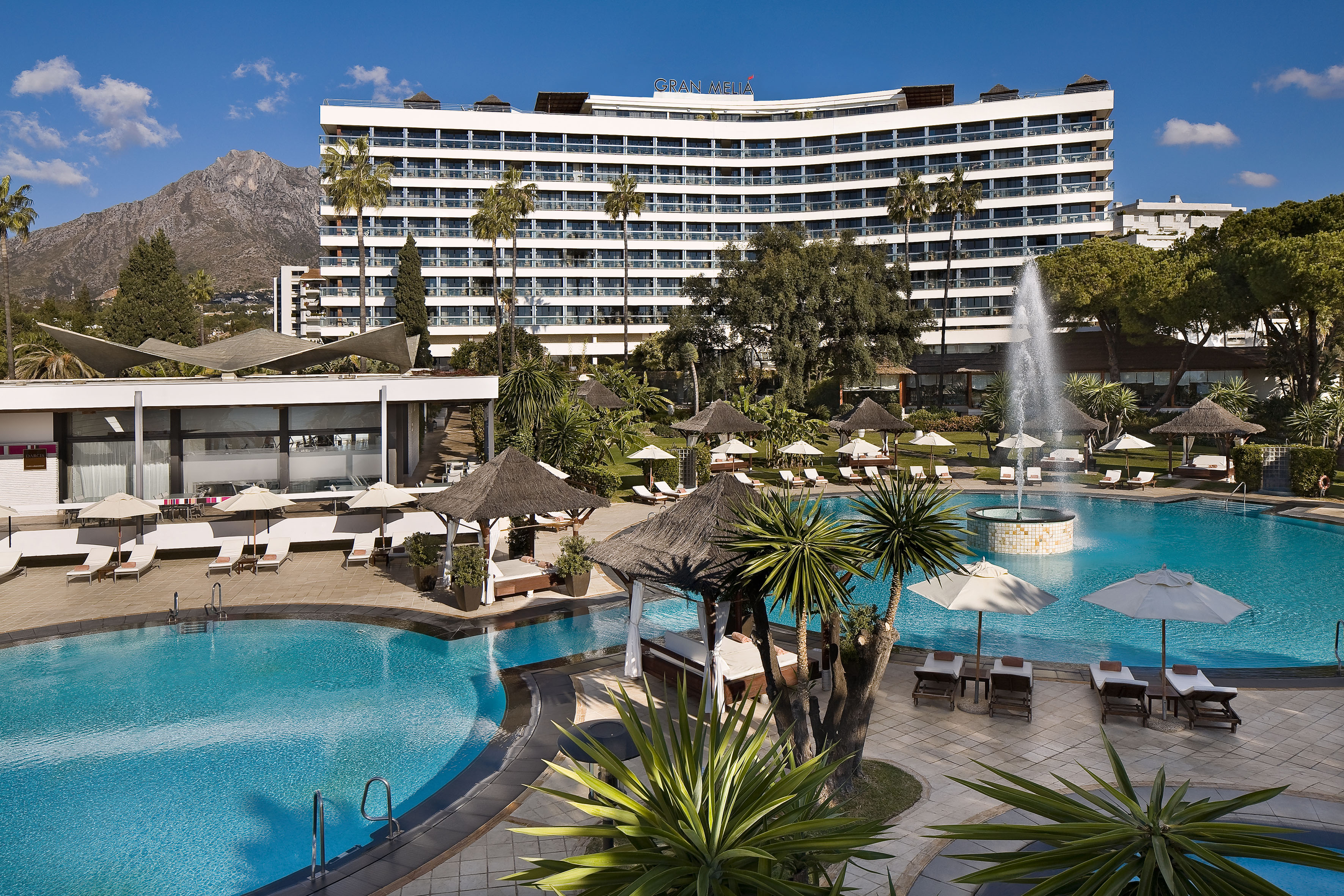 Gran Melia resort pool, sun loungers, fountain, palm trees, and mountain view.