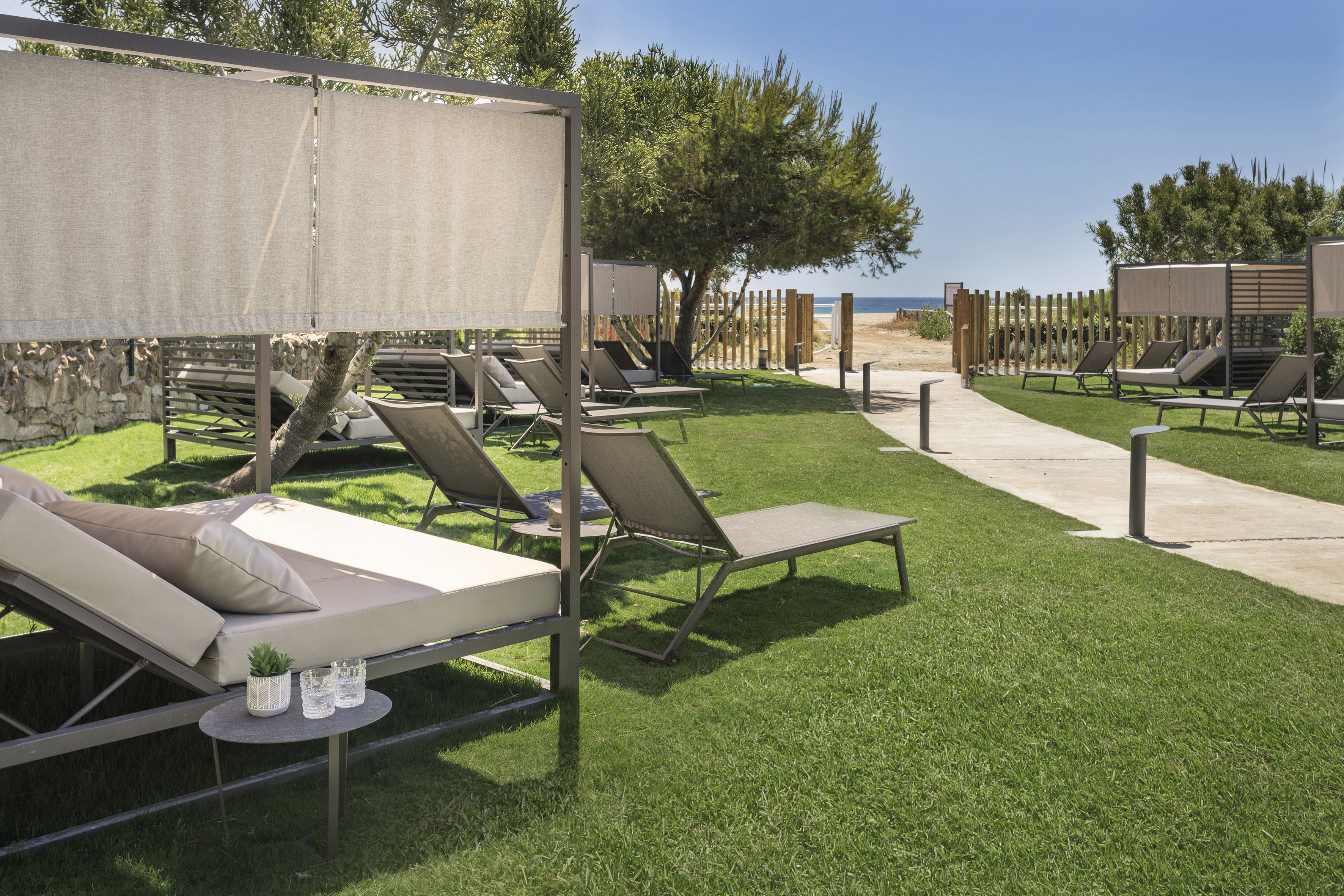 Coastal resort lounge area with sunbeds and path to the beach.