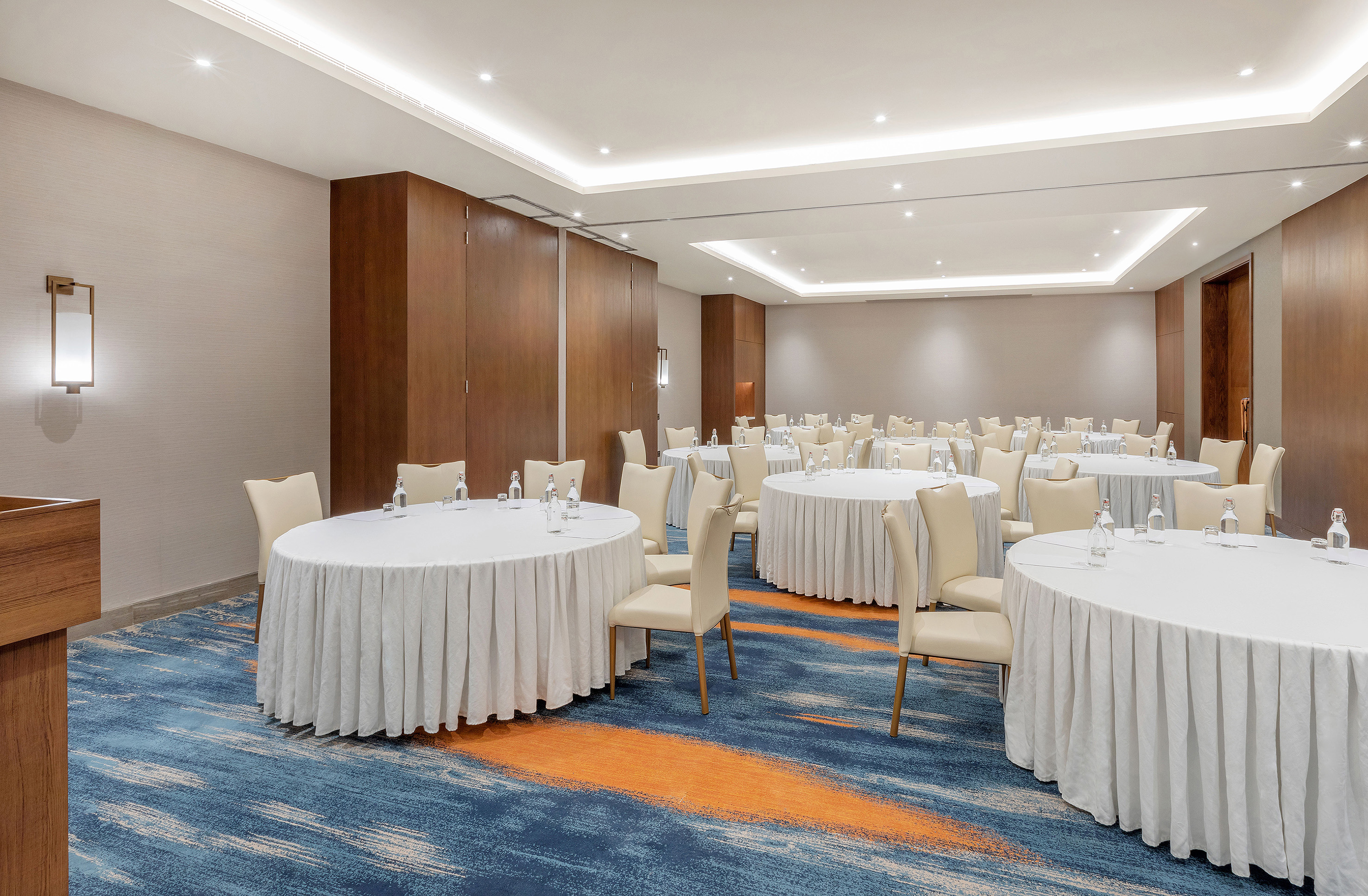 Modern conference room with round tables, beige chairs, and patterned carpet.