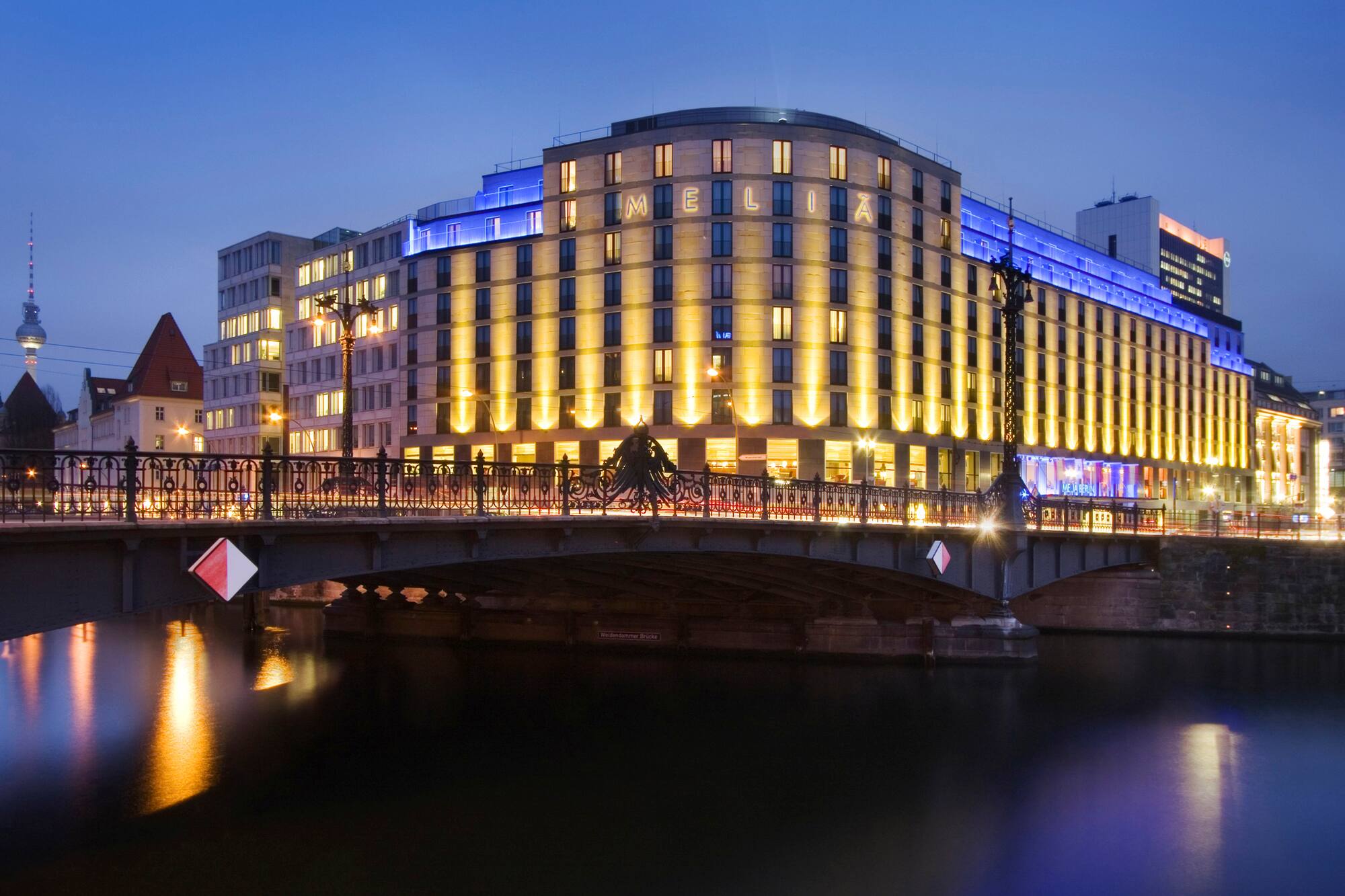 Illuminated Melia Berlin Hotel and bridge over Spree River at dusk, with TV Tower.
