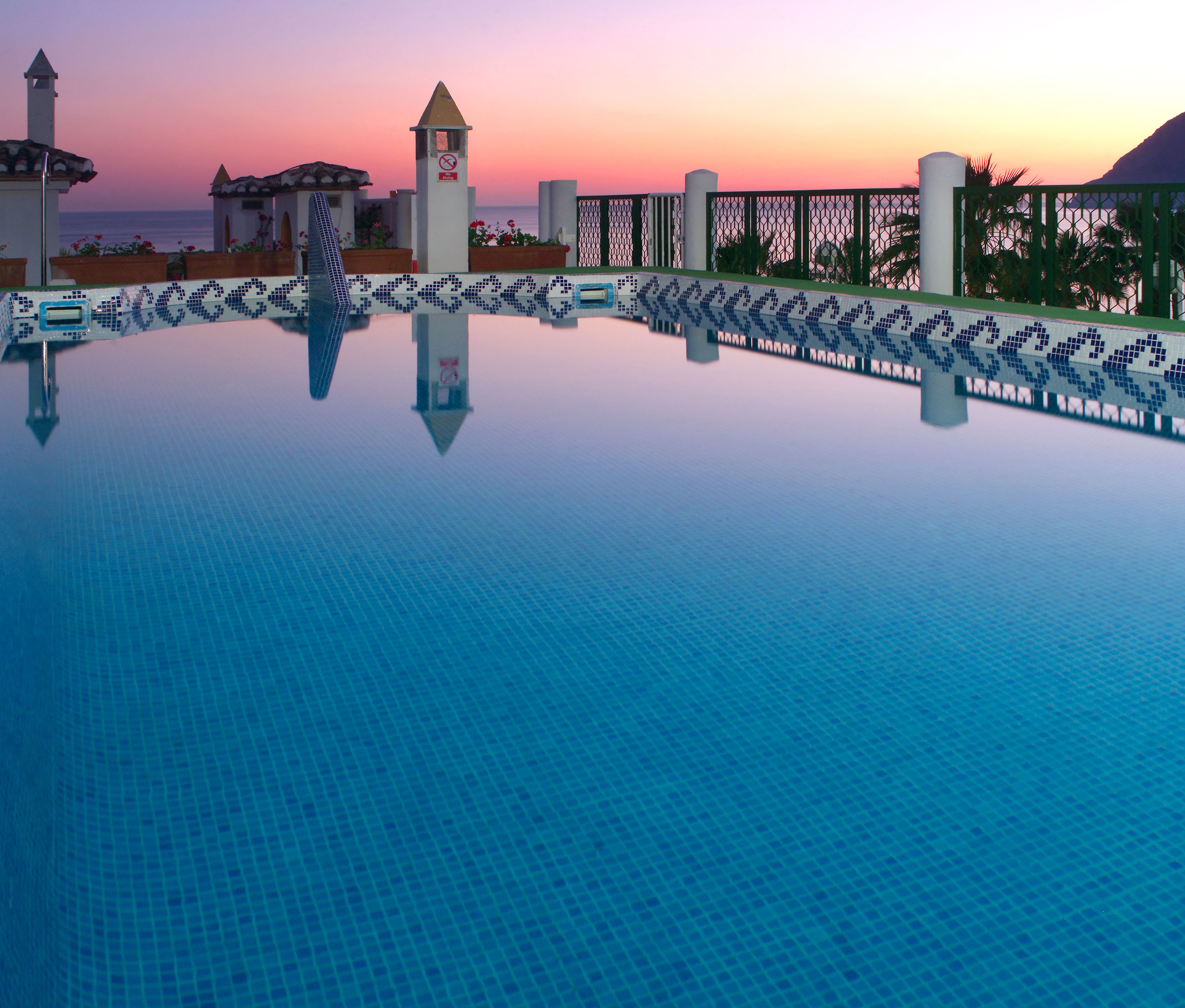 Resort swimming pool reflecting vibrant sunset colors over the ocean.