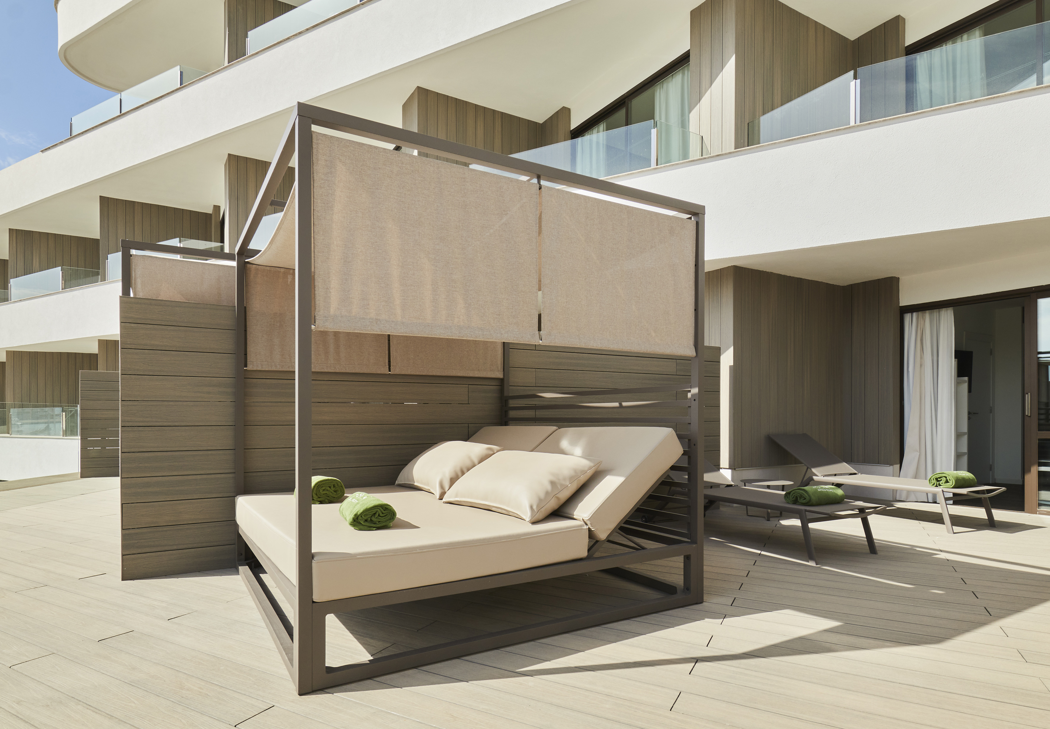 Modern hotel terrace with canopy daybed, sun loungers, and wooden decking.