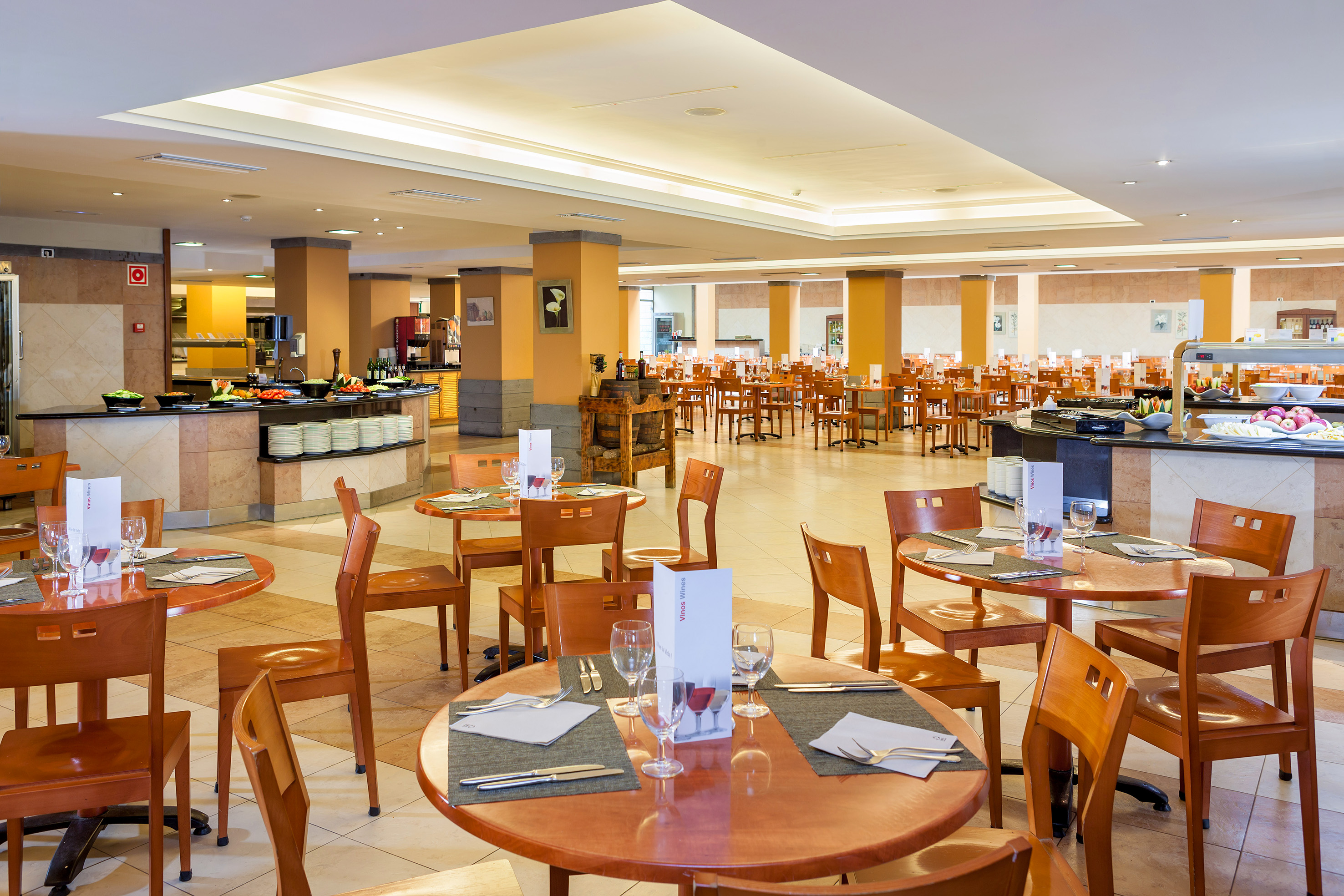 Spacious hotel buffet restaurant with set wooden tables and food bars.