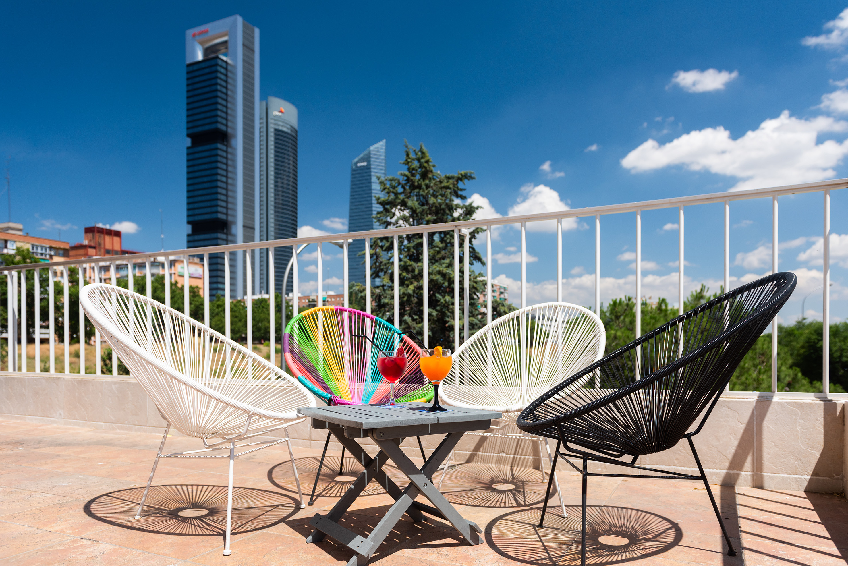 Sunny terrace with modern Acapulco chairs, cocktails, and Madrid skyscraper views.
