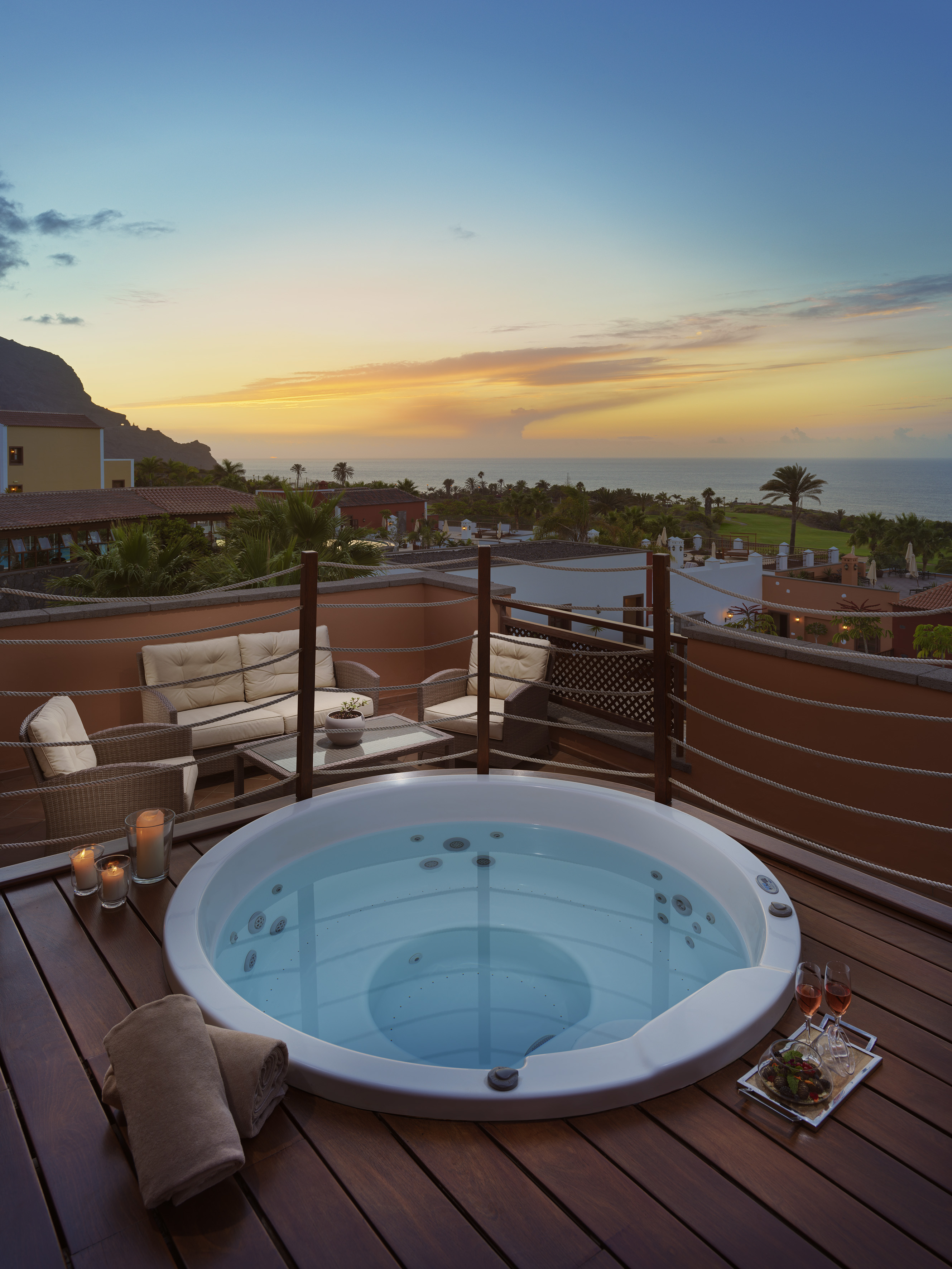 Luxury hot tub on resort balcony at sunset with ocean and mountain views.