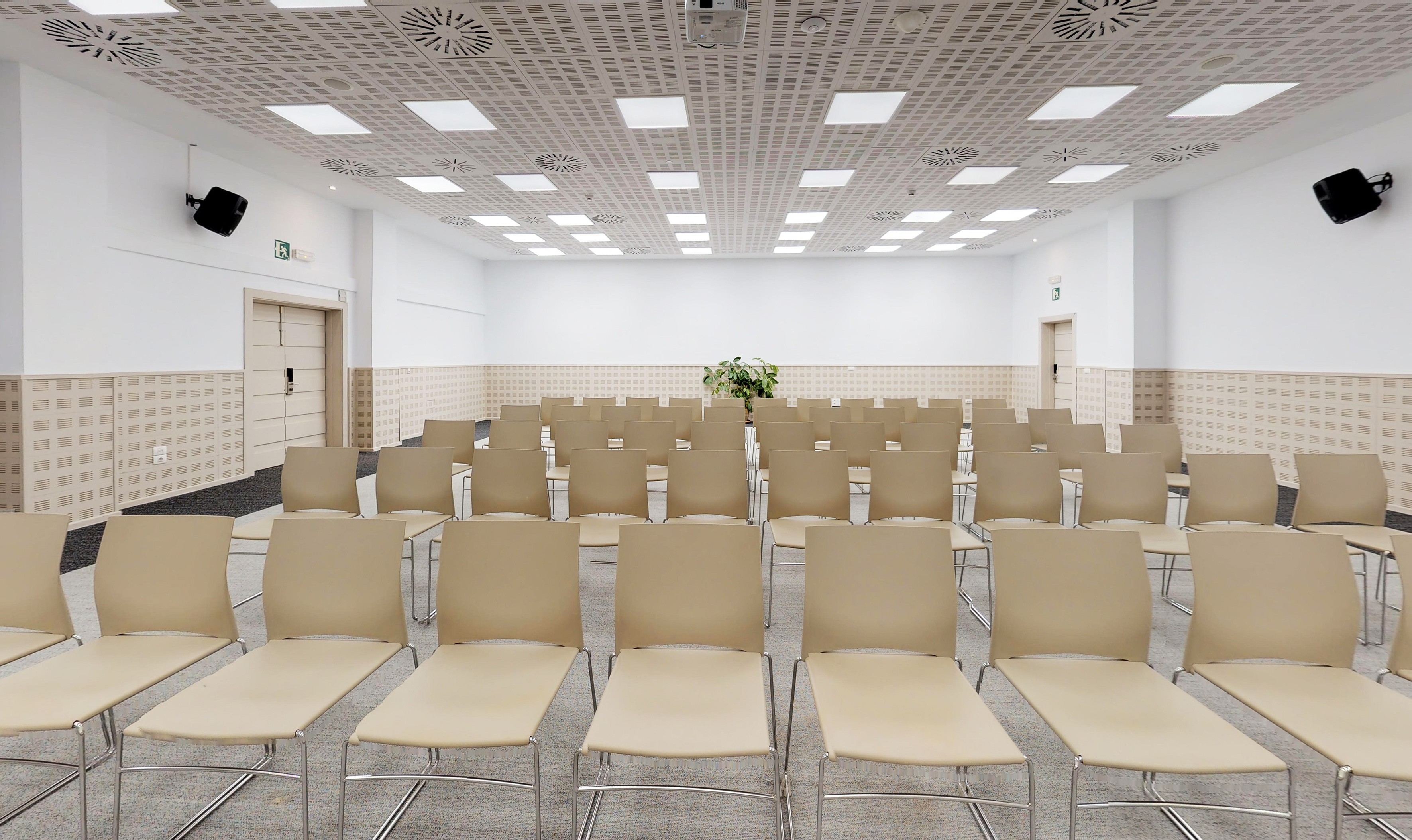 Empty conference room with rows of beige chairs, white walls, and modern ceiling.