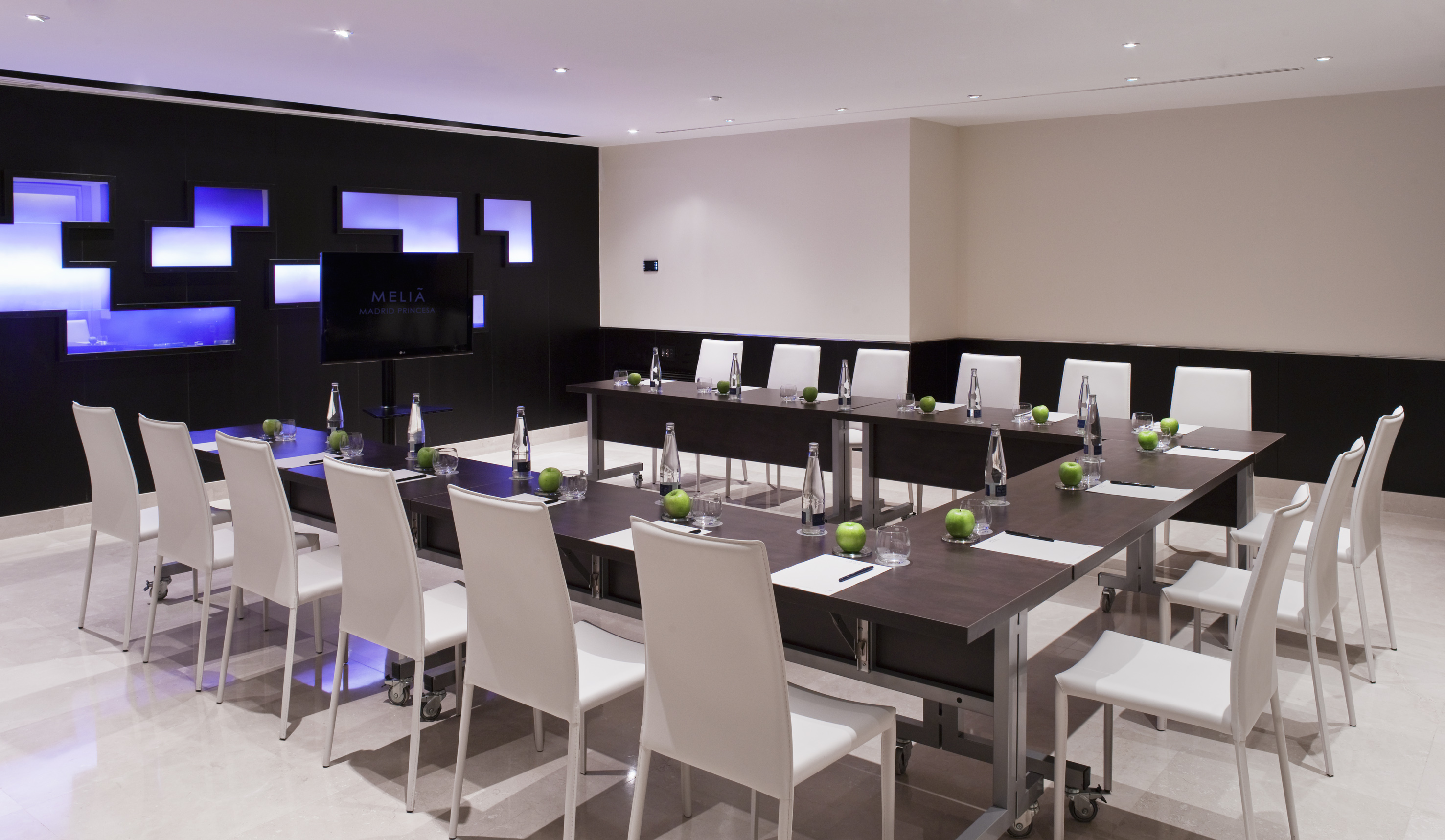 Melia hotel conference room with U-shaped table, white chairs, and TV.