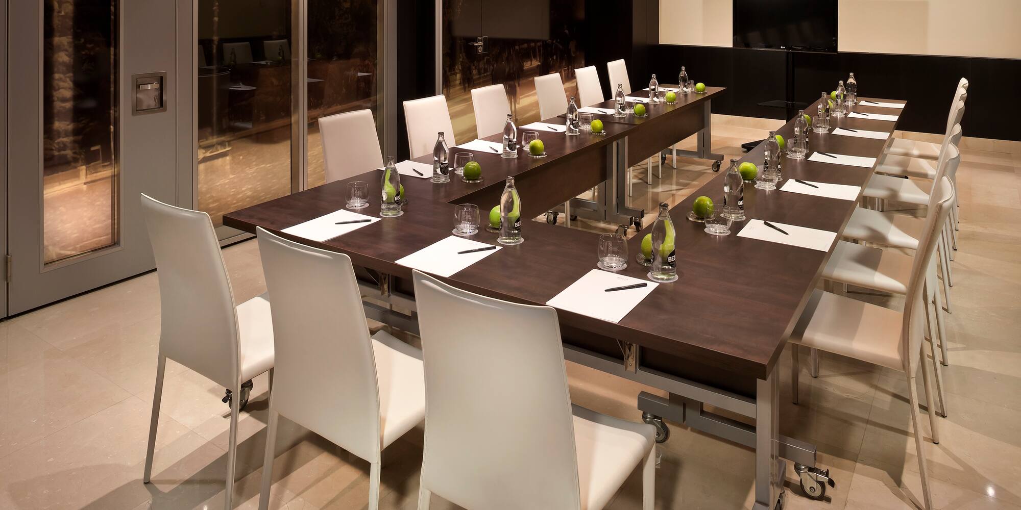 a long table with white chairs and a glass wall