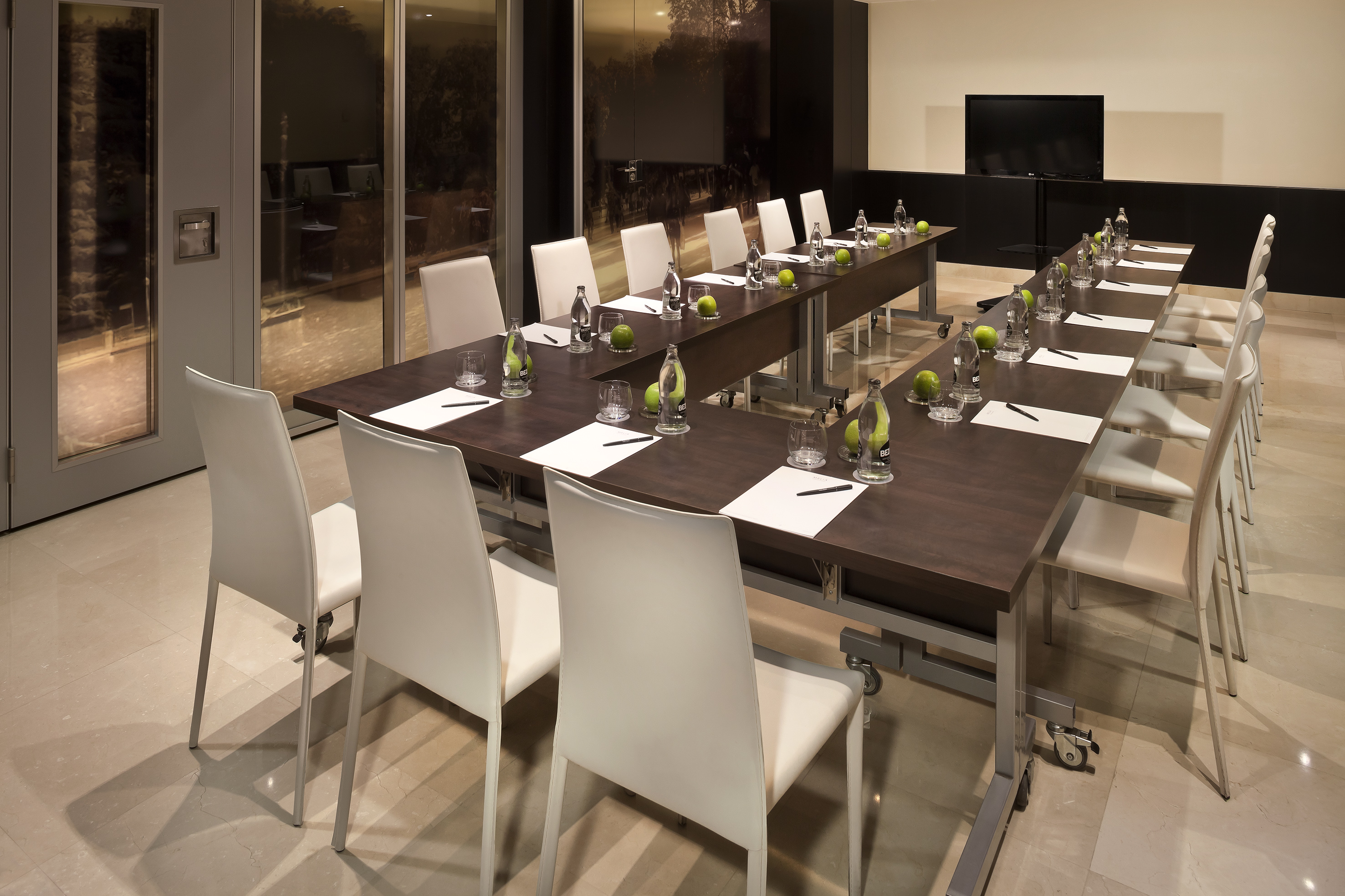 Modern conference room with U-shaped table, white chairs, and large TV.