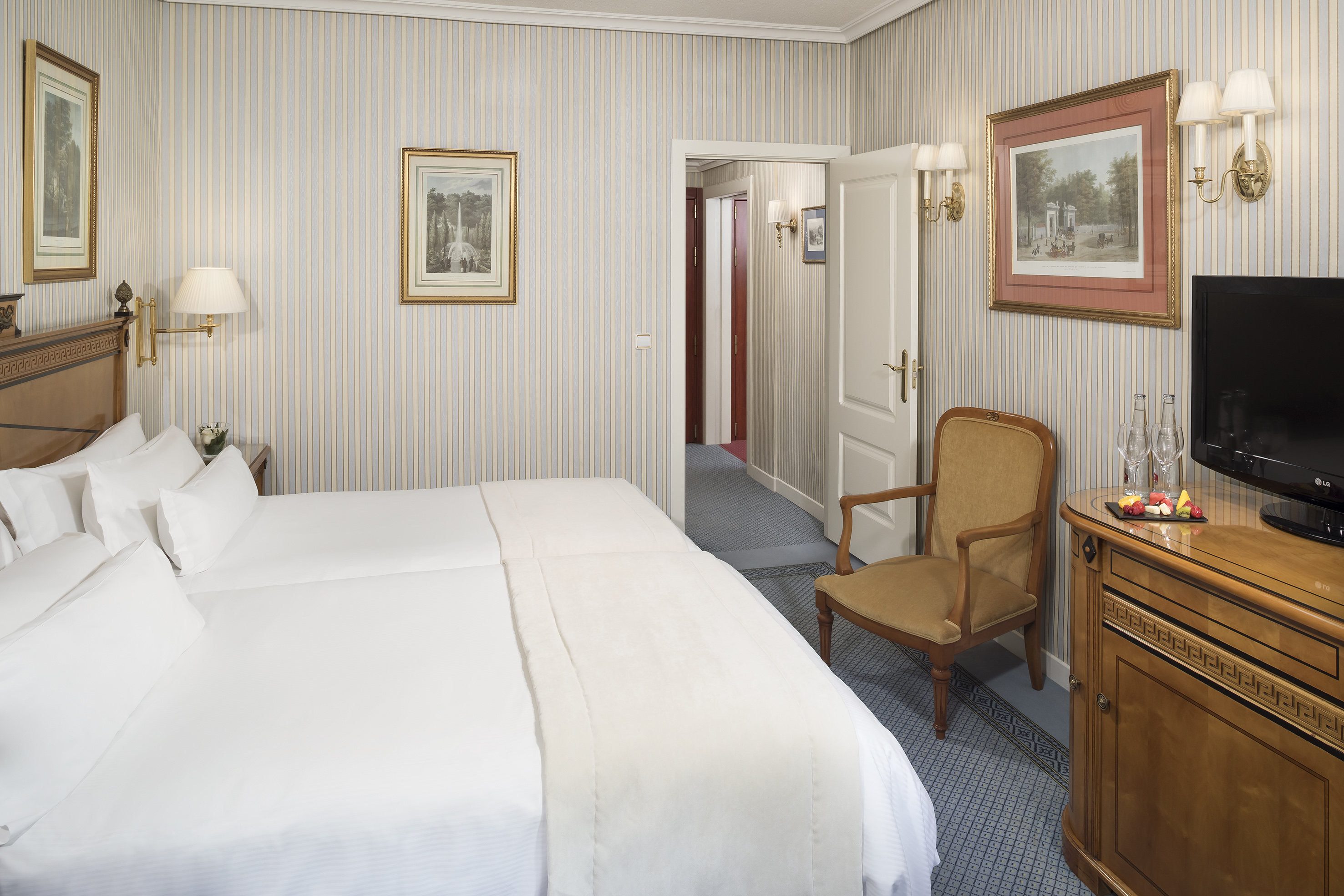 Hotel room with twin beds, striped walls, wooden furniture, and classic decor.