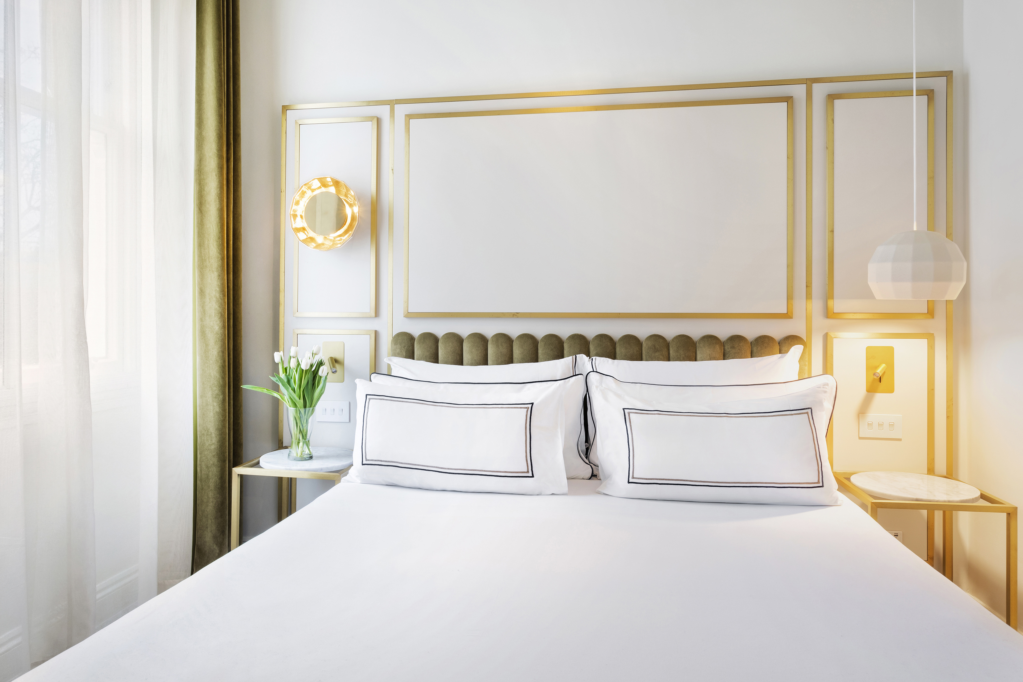 Modern bedroom with white bed, olive velvet headboard, and gold frame accents.