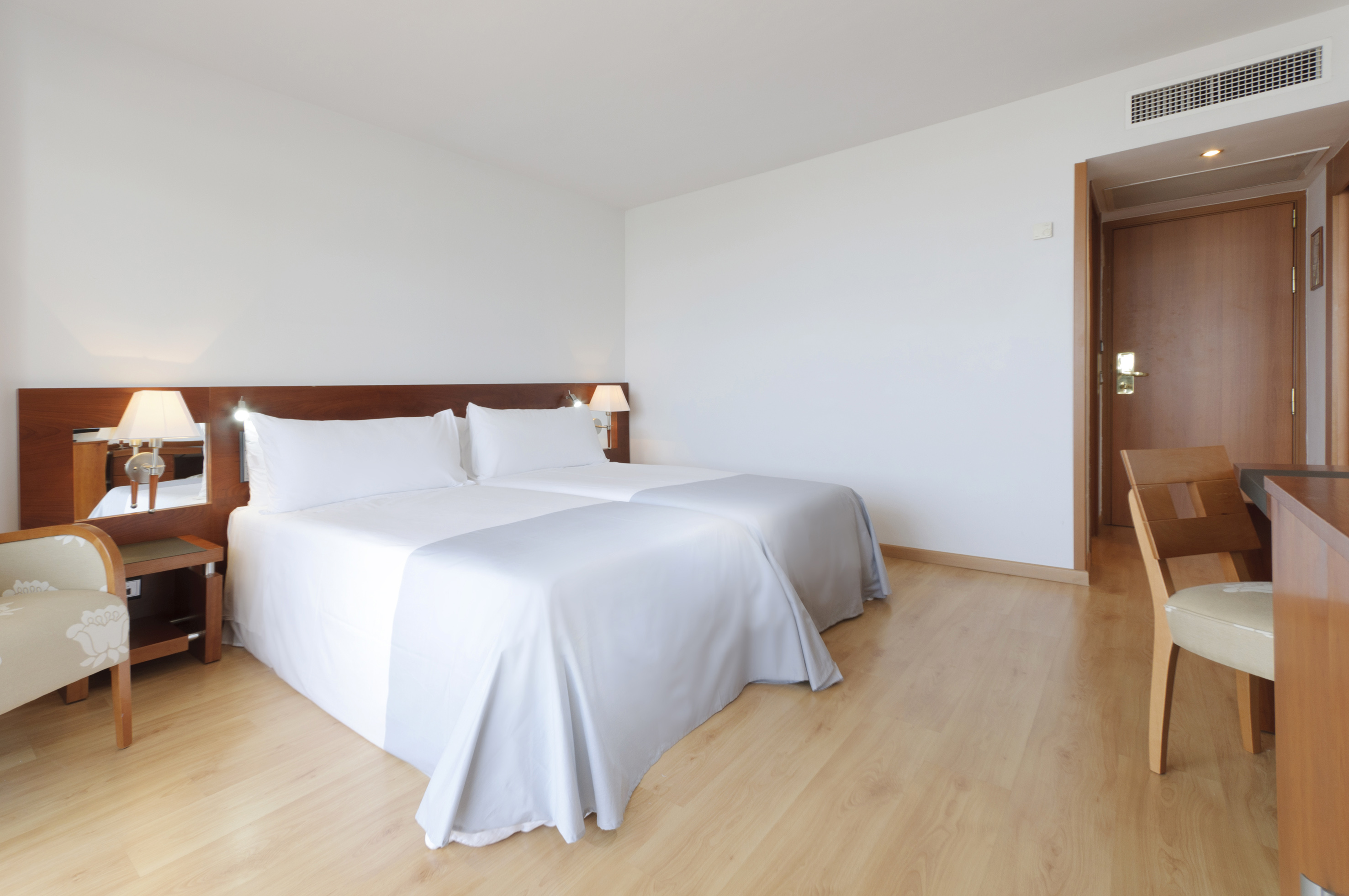 Bright hotel room with twin beds, white linens, wooden floor, and modern design.