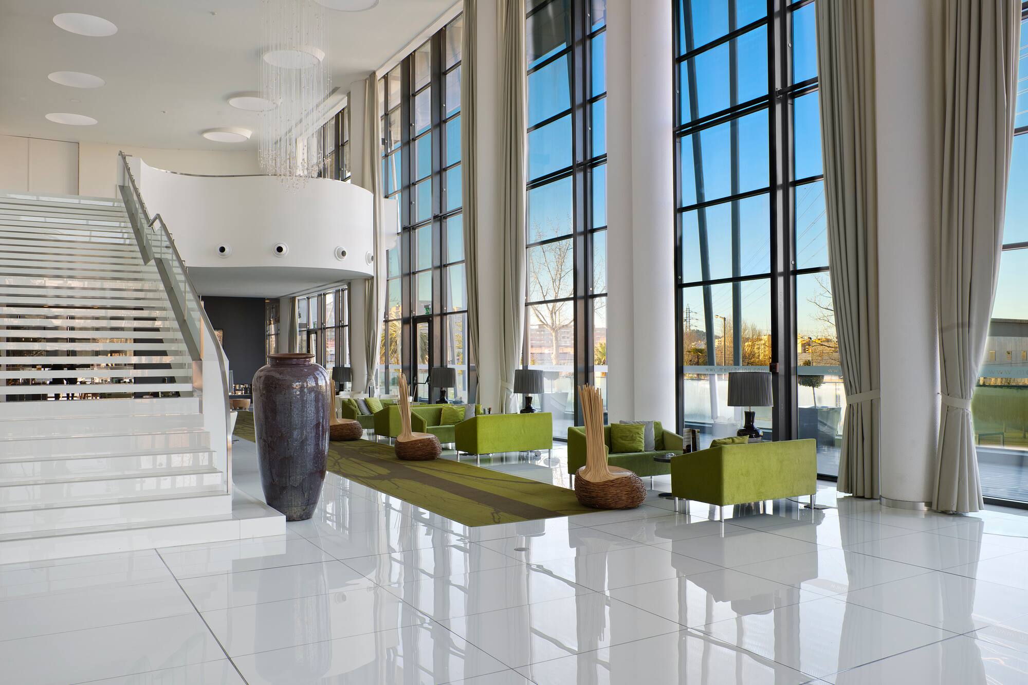 Hotel lobby with white staircase, green lounge sofas, and floor-to-ceiling windows.