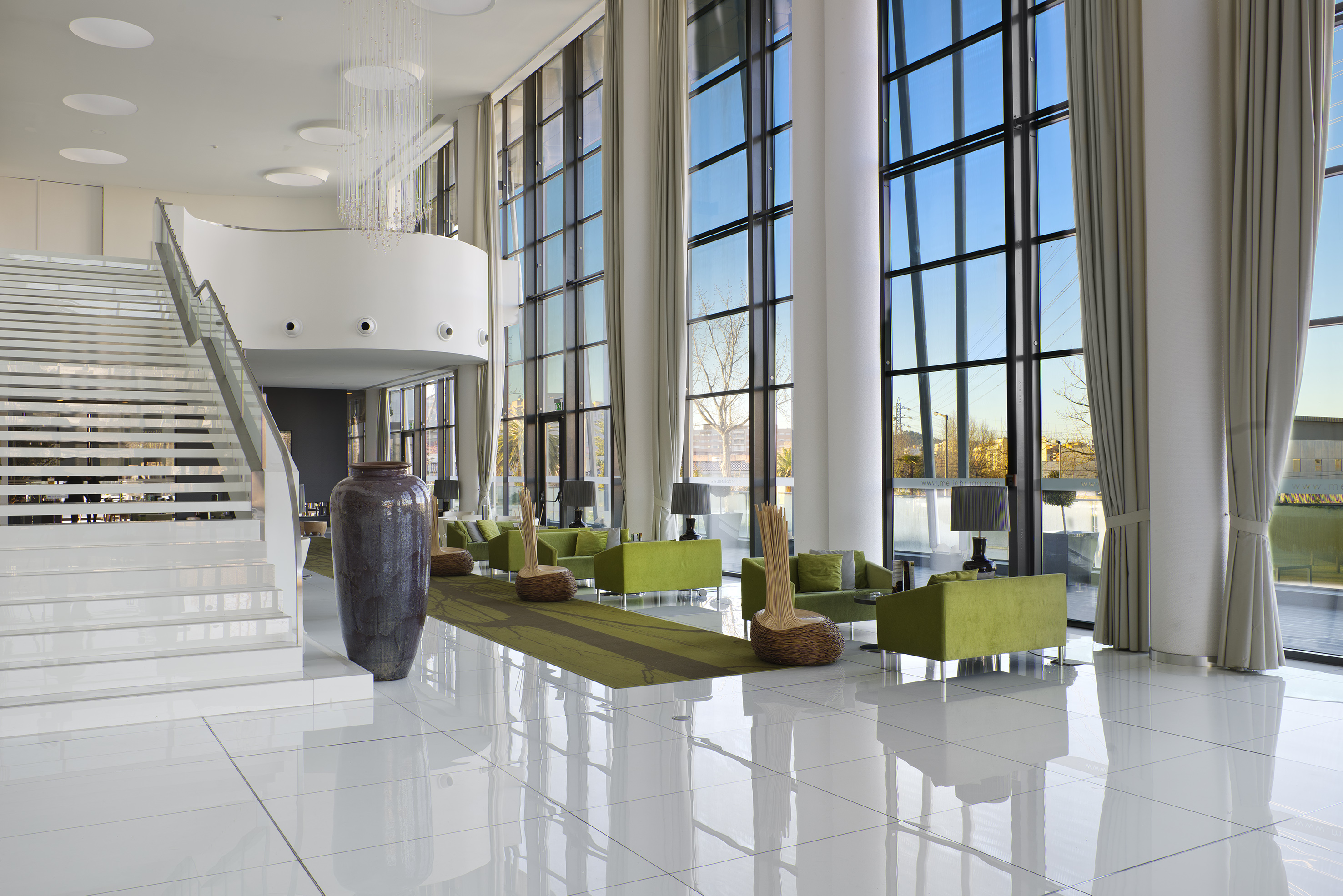 Hotel lobby with white staircase, green lounge sofas, and floor-to-ceiling windows.