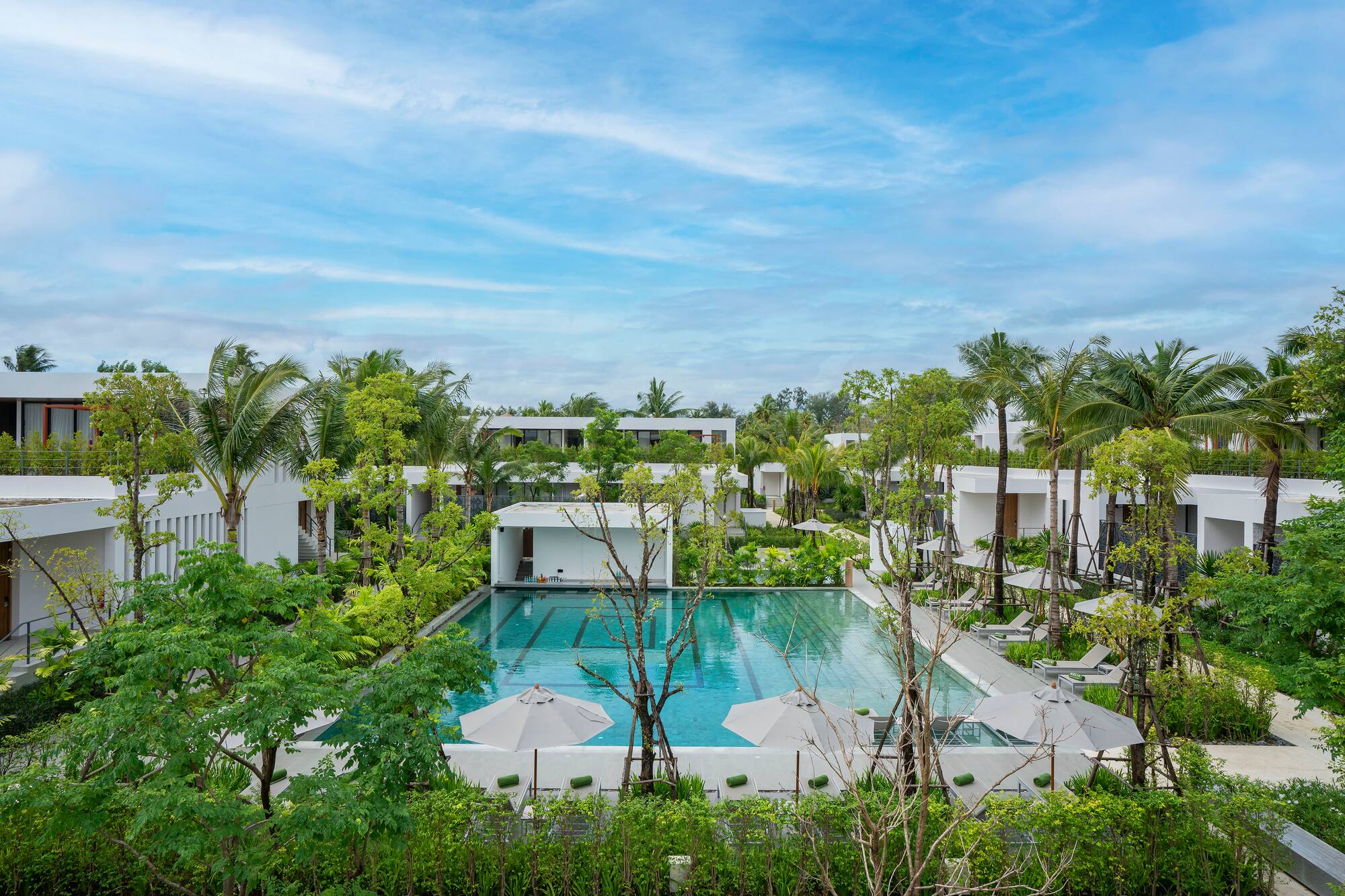 Tropical resort with a large swimming pool, modern buildings, and palm trees.