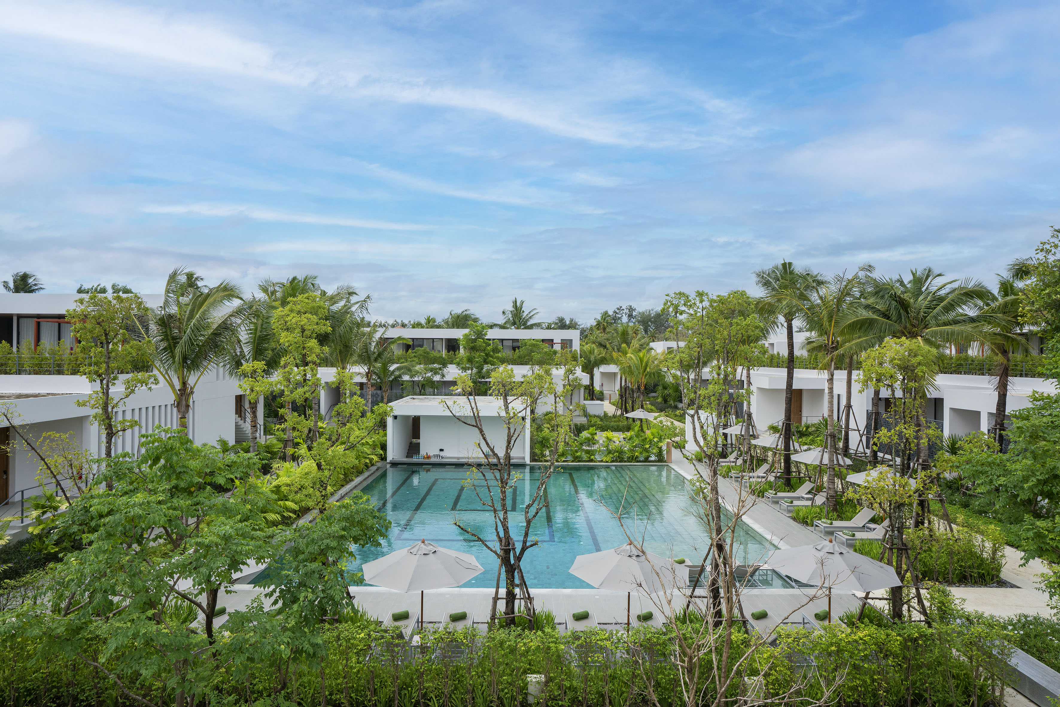 Tropical resort with a large swimming pool, modern buildings, and palm trees.