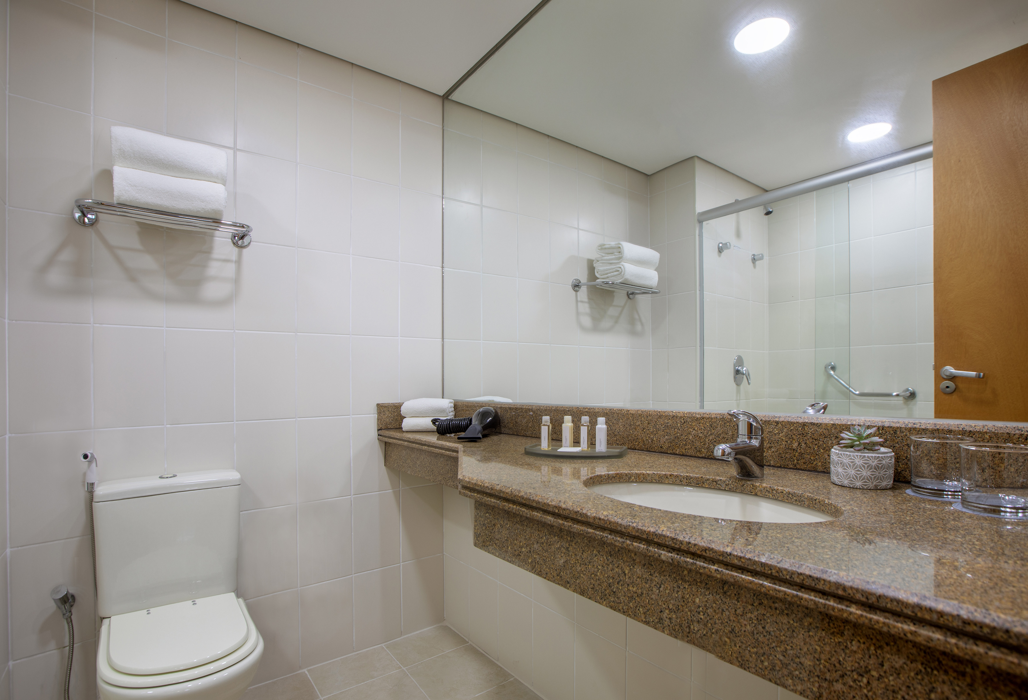 Bright, clean hotel bathroom with granite vanity, sink, toilet, and shower.