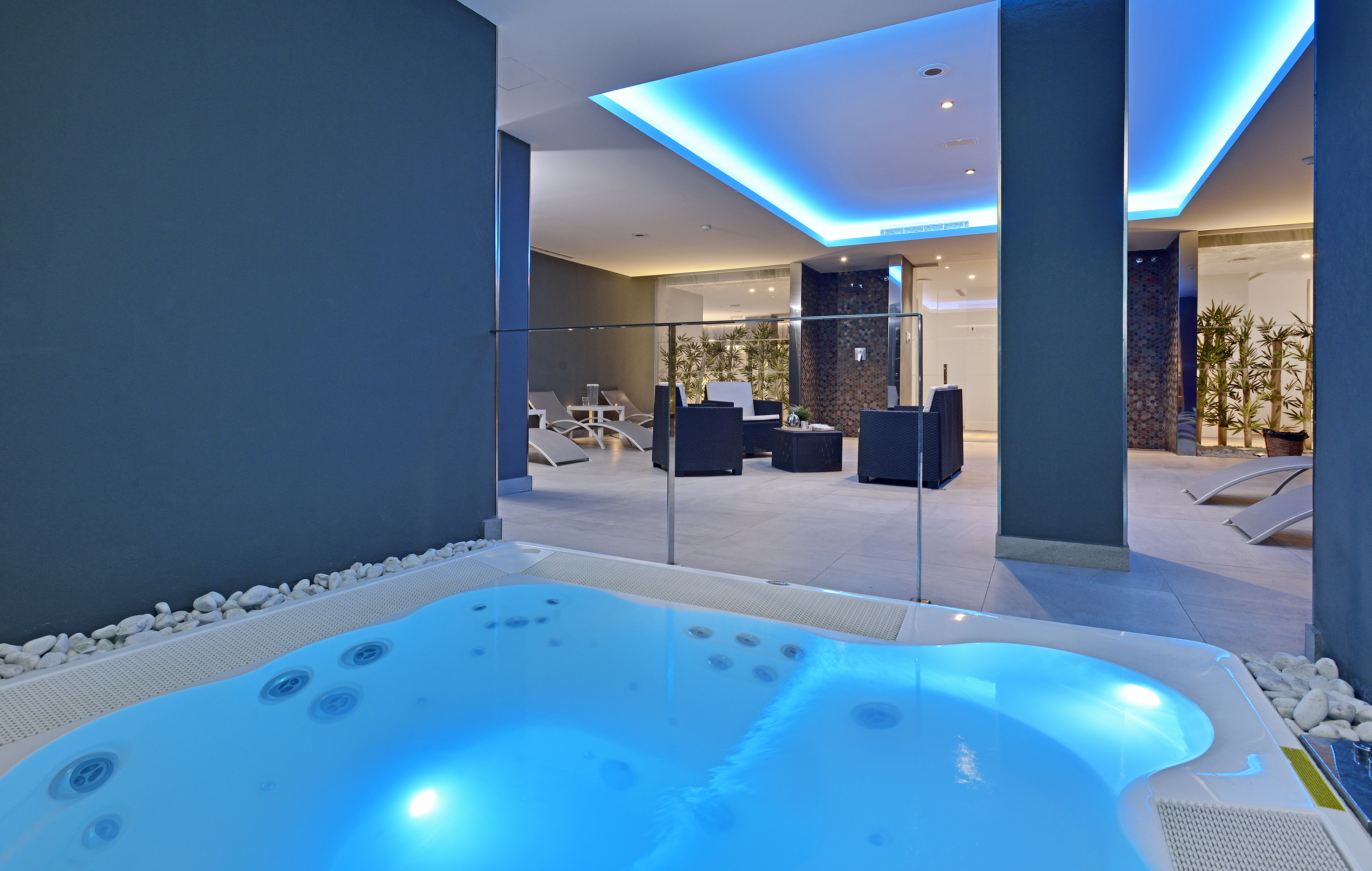Indoor spa with illuminated jacuzzi, relaxation chairs, and bamboo decor.