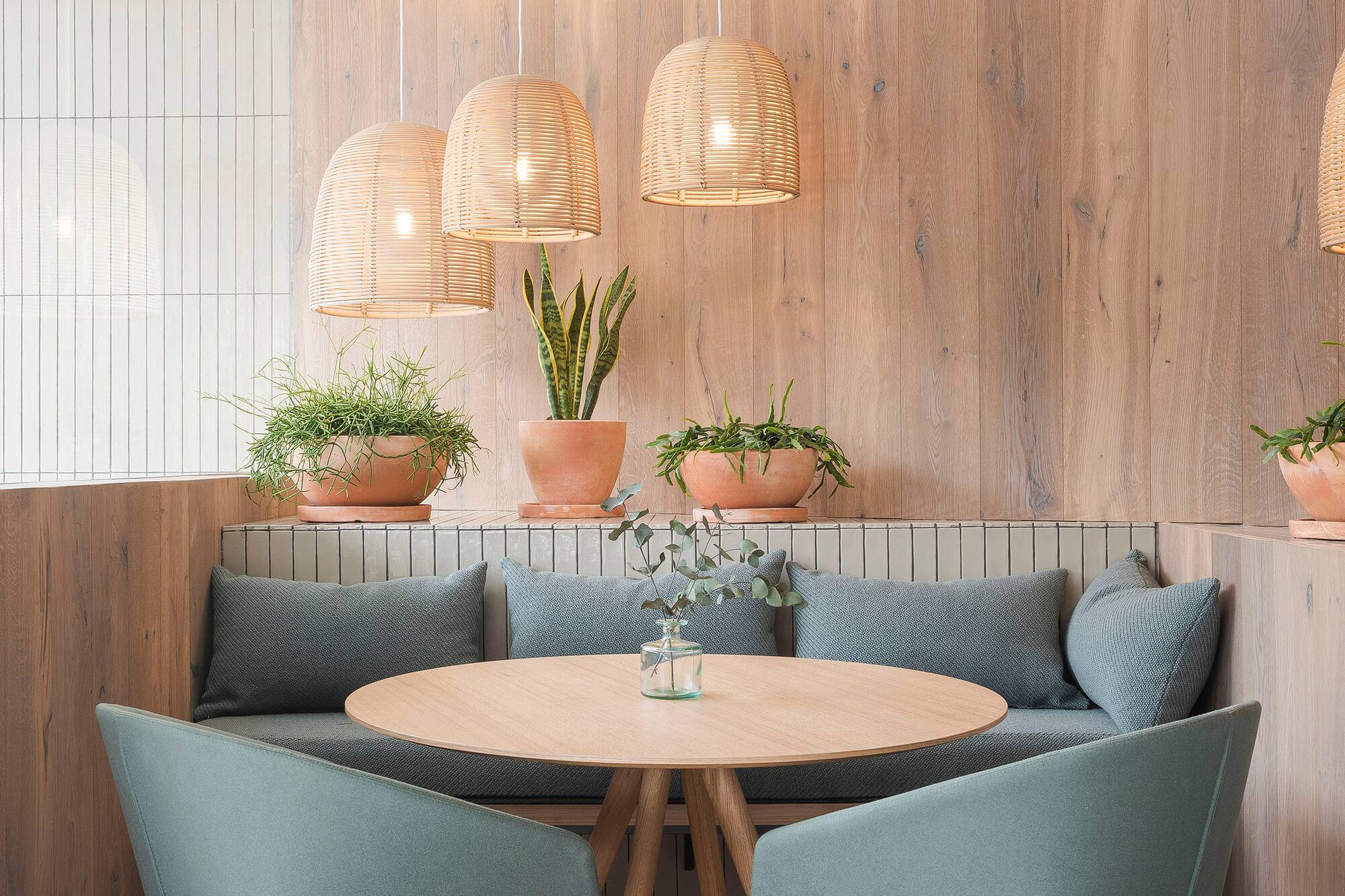 Cafe booth with round wood table, green chairs, wicker pendant lights, and plants.