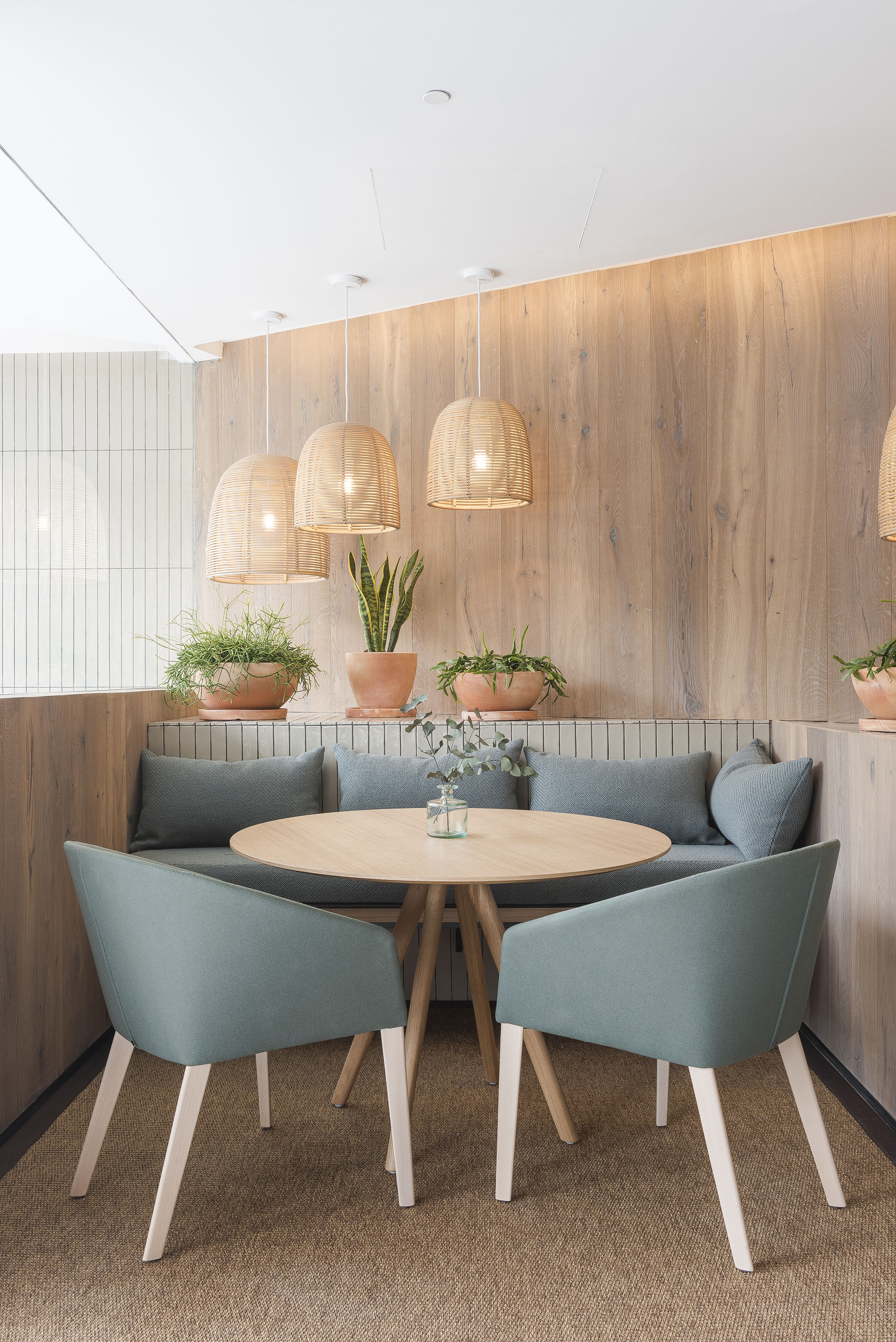 Cafe booth with round wood table, green chairs, wicker pendant lights, and plants.
