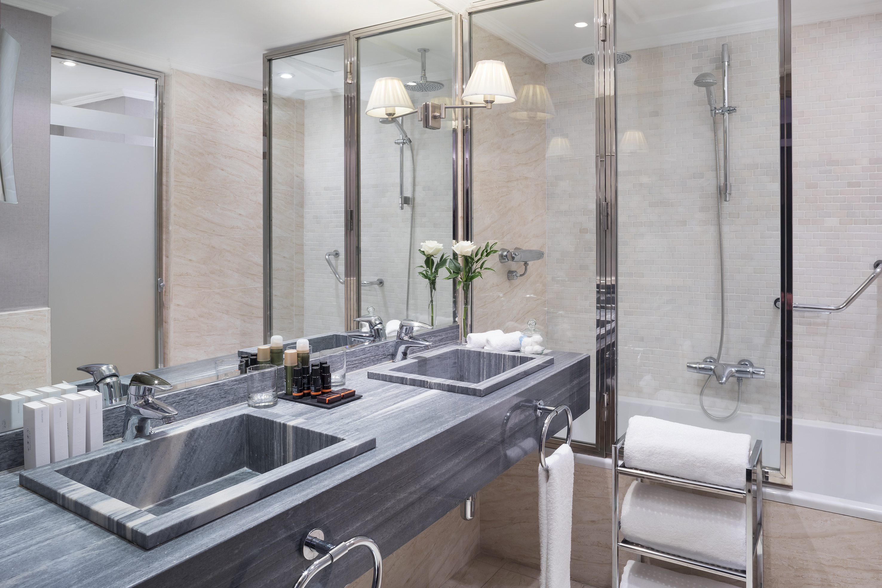 Elegant hotel bathroom with double grey marble vanity, shower, and tub.