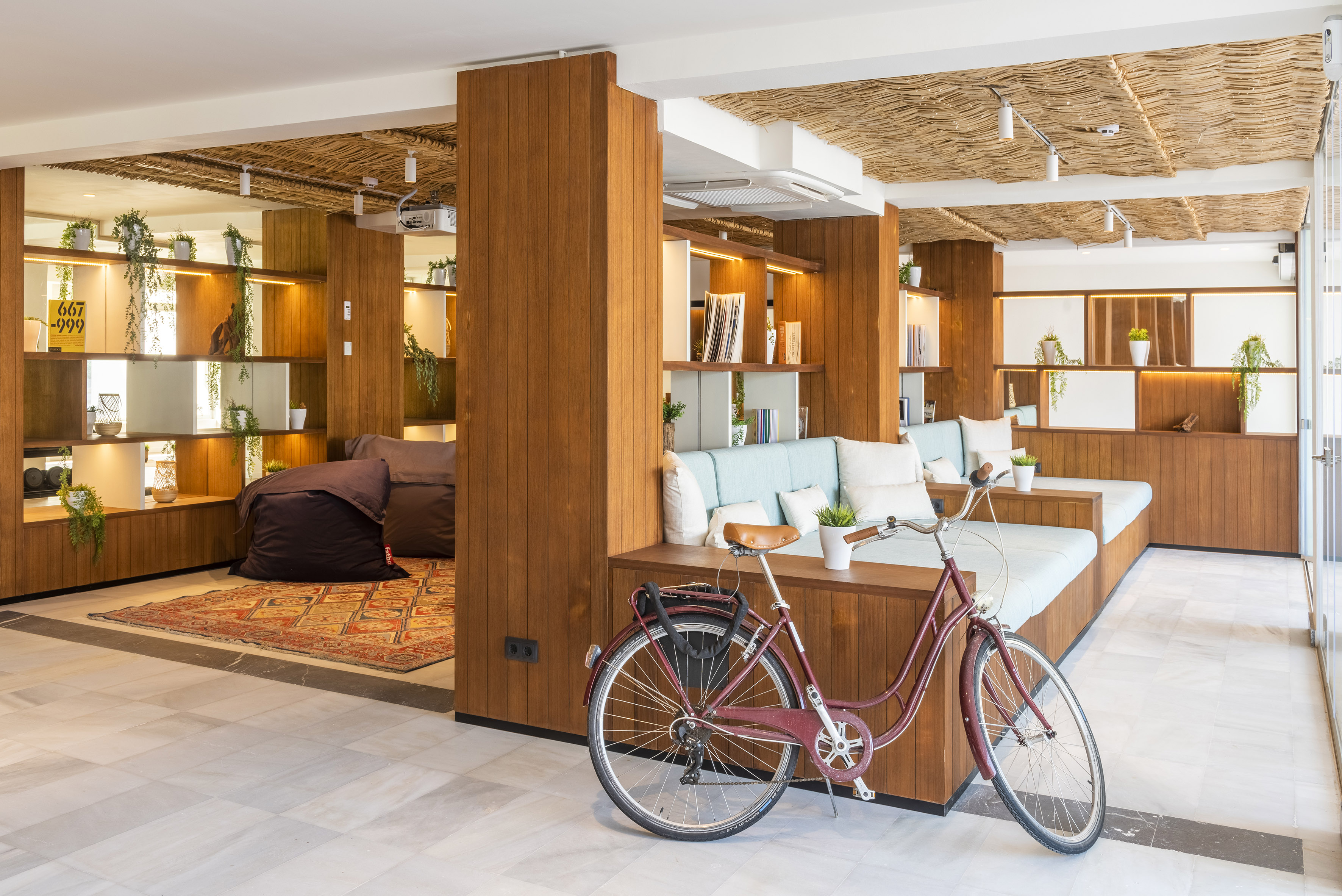 Hotel lounge with wood panels, plants, light sofas, straw ceiling, and vintage bike.