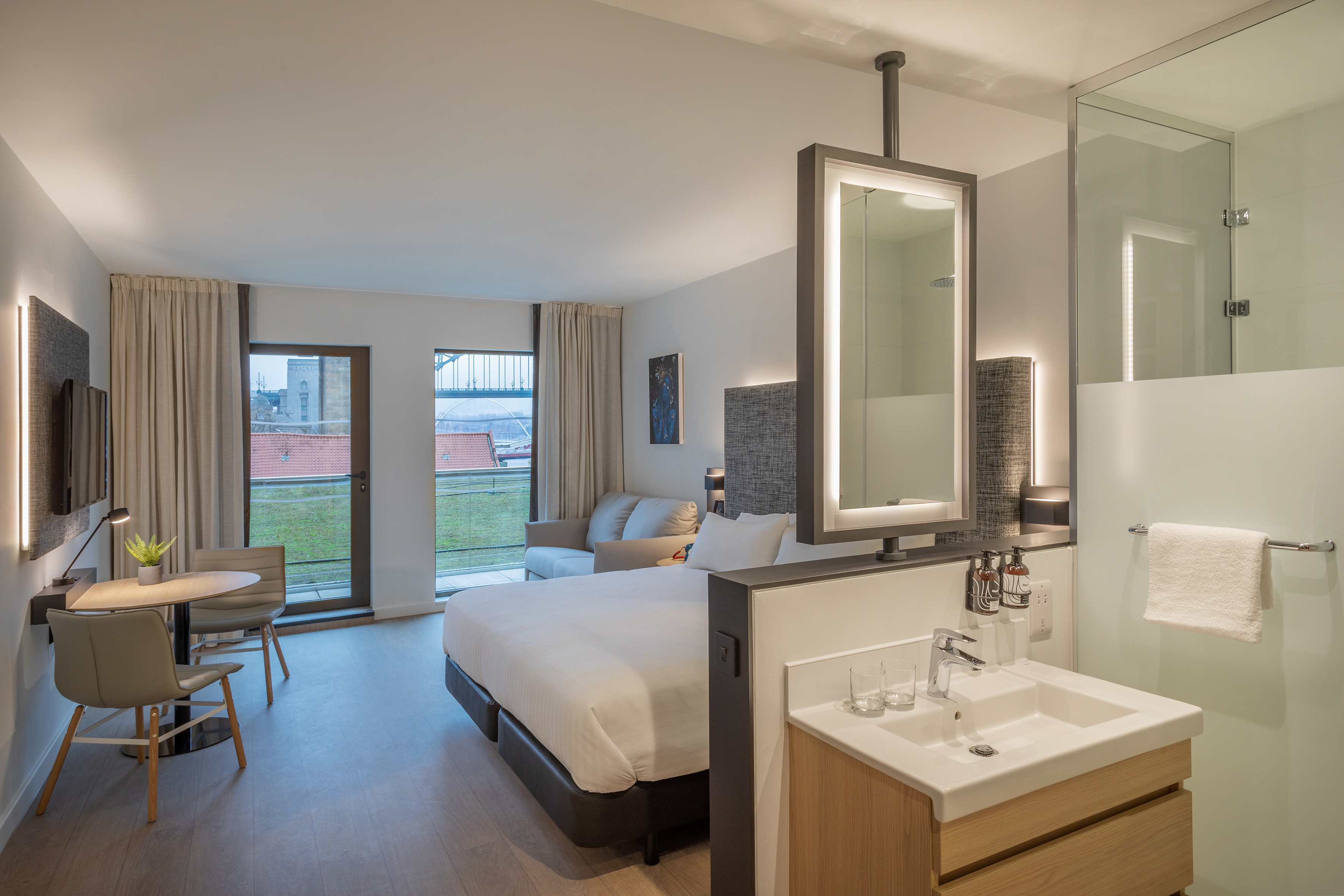 Modern studio hotel room with bed, sofa, table, integrated bathroom, and city view.