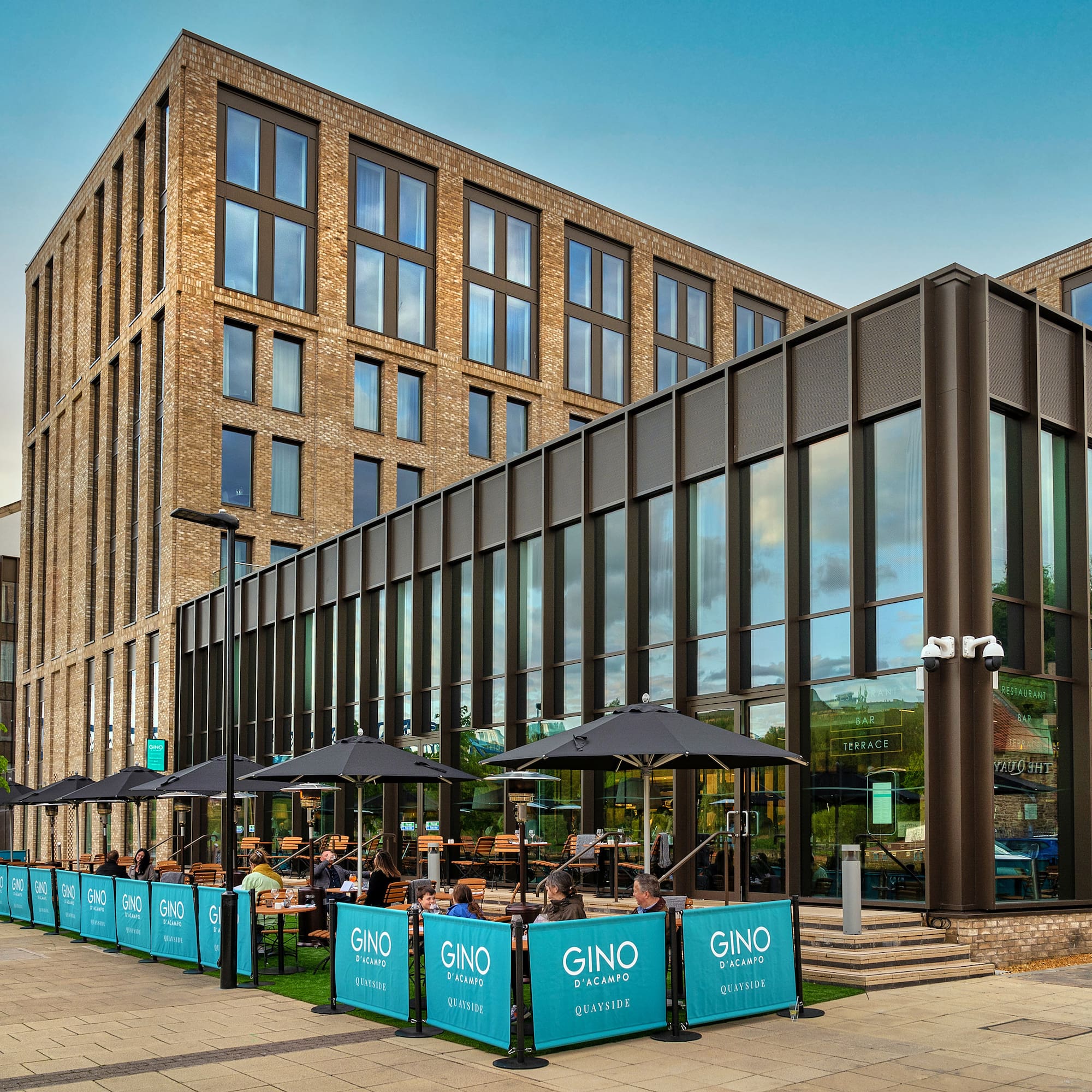 Modern hotel building, Gino D'Acampo Quayside restaurant outdoor terrace with diners.