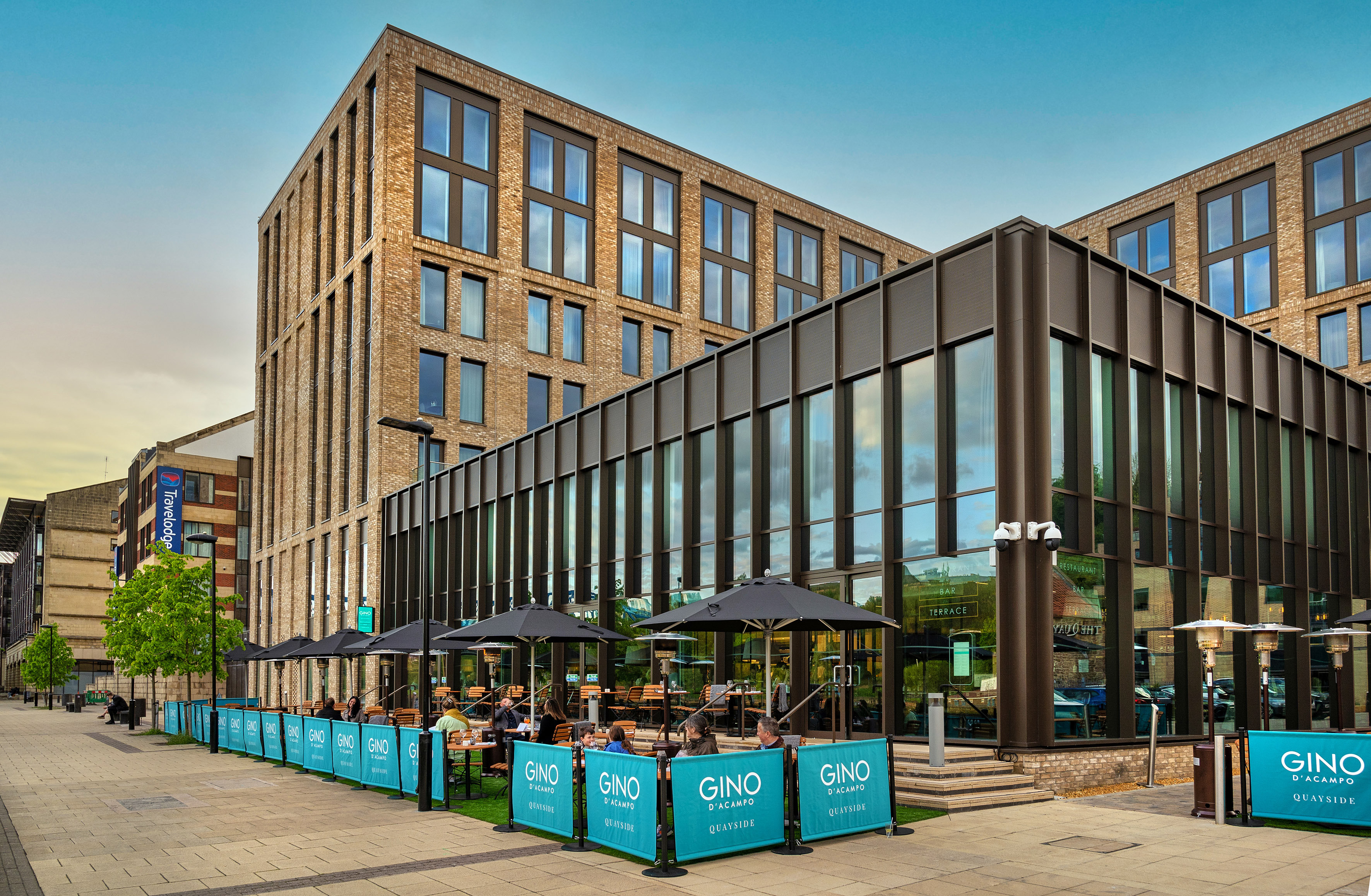 Modern brick hotel and Gino D'Acampo Quayside restaurant terrace with diners.