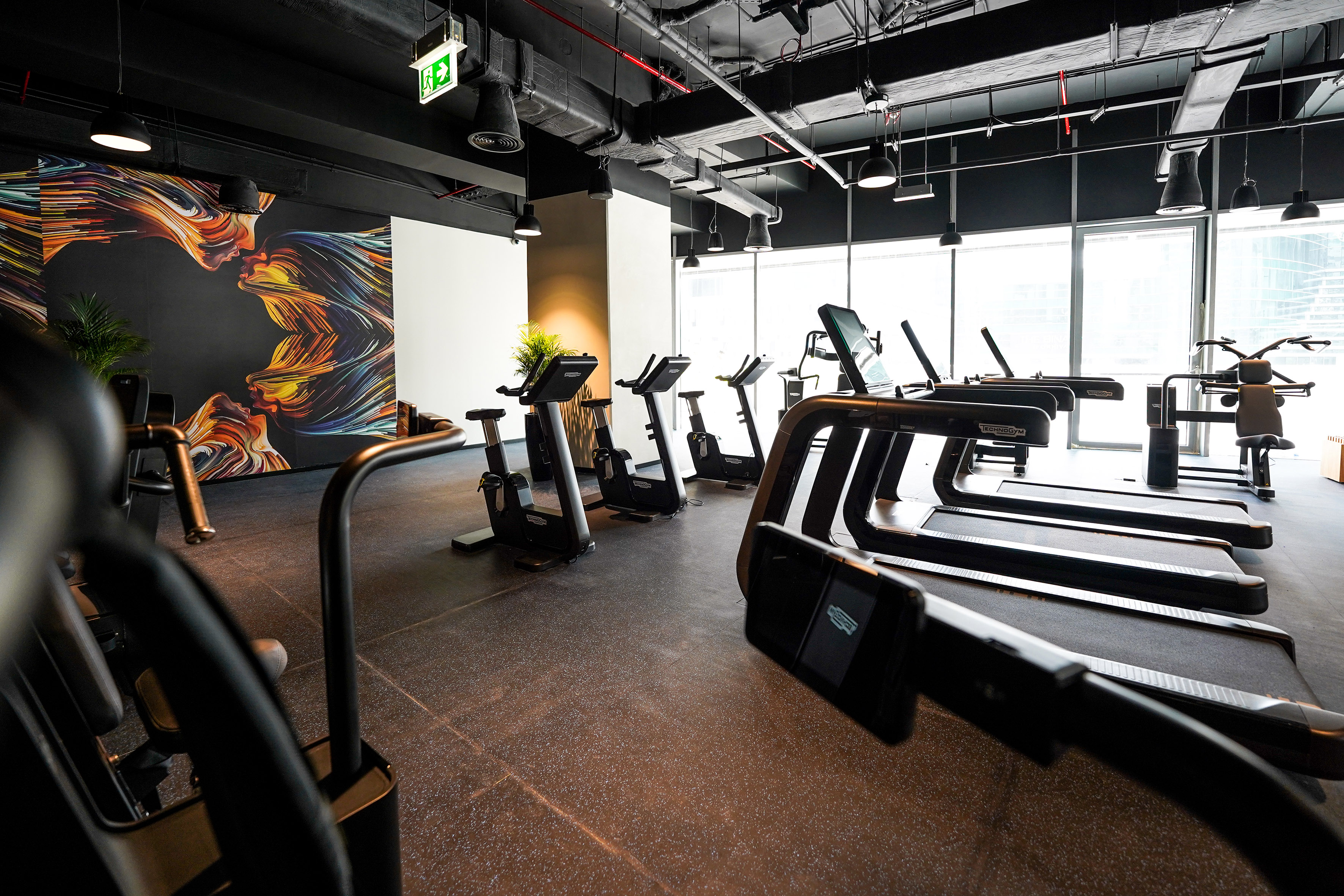Sleek gym interior with Technogym equipment, colorful mural, and industrial ceiling.