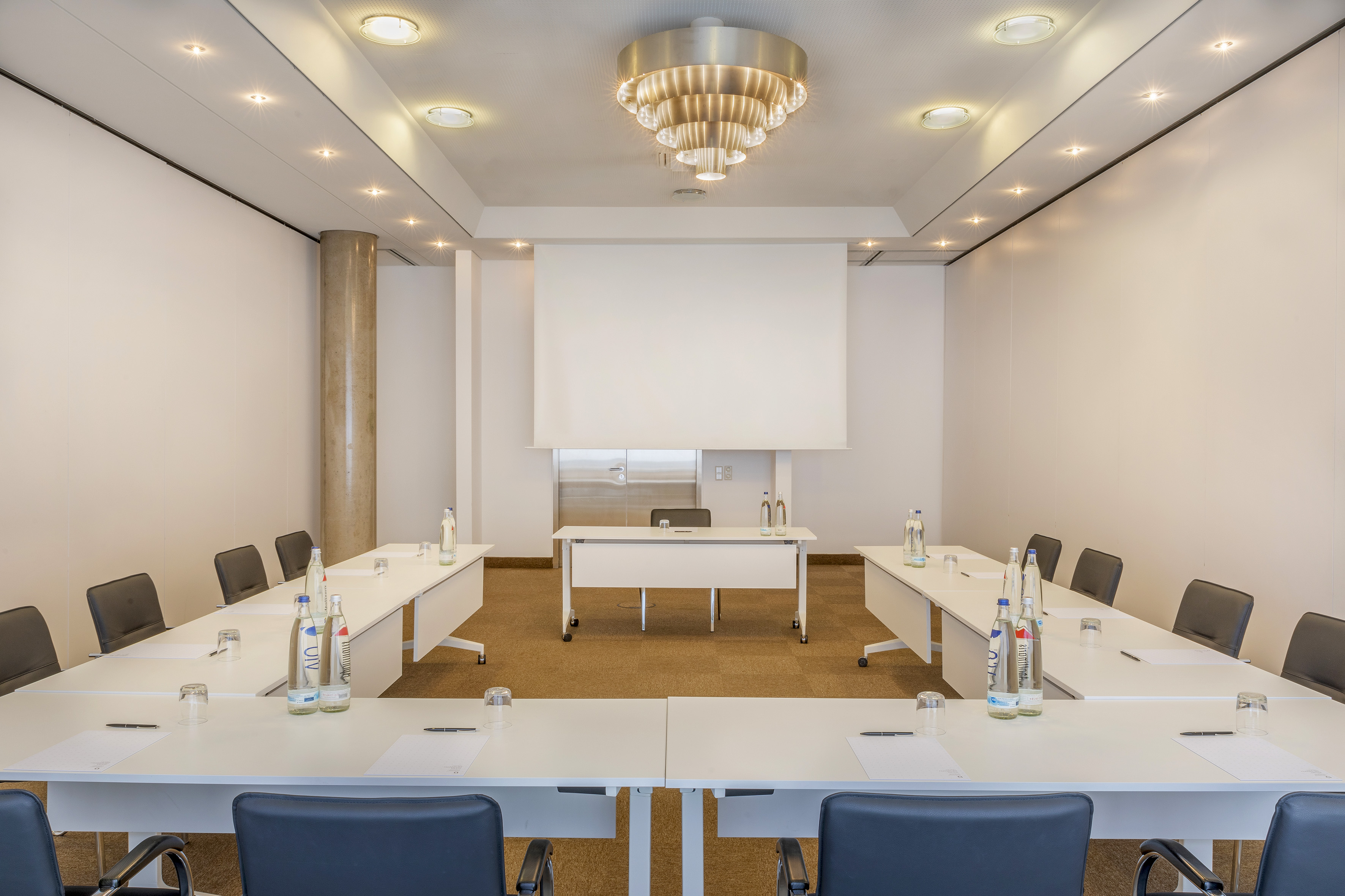 Modern conference room with U-shaped table setup and projector screen.