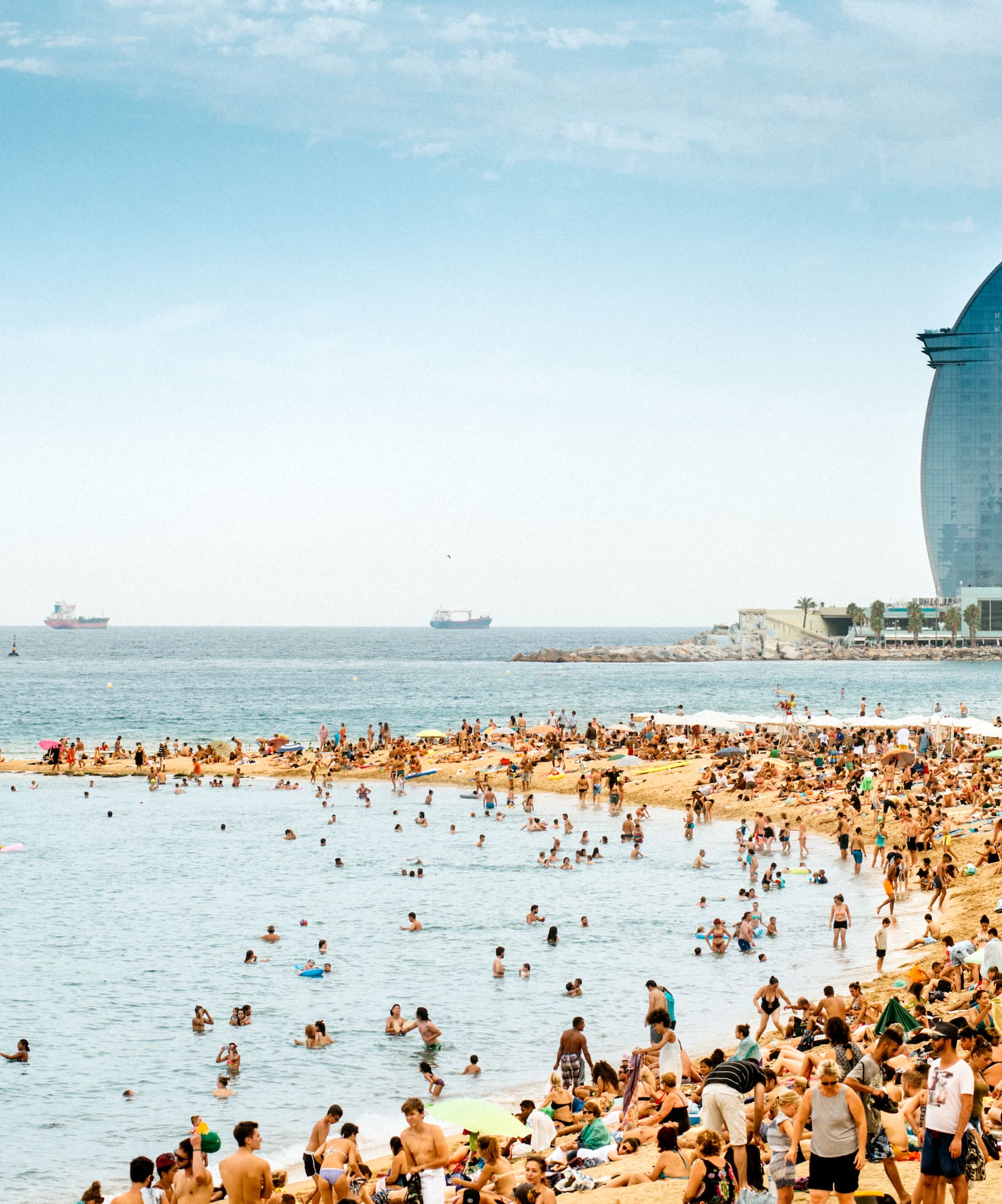 Bañistas en la concurrida playa de Barcelona, Hotel Vela y mar azul.