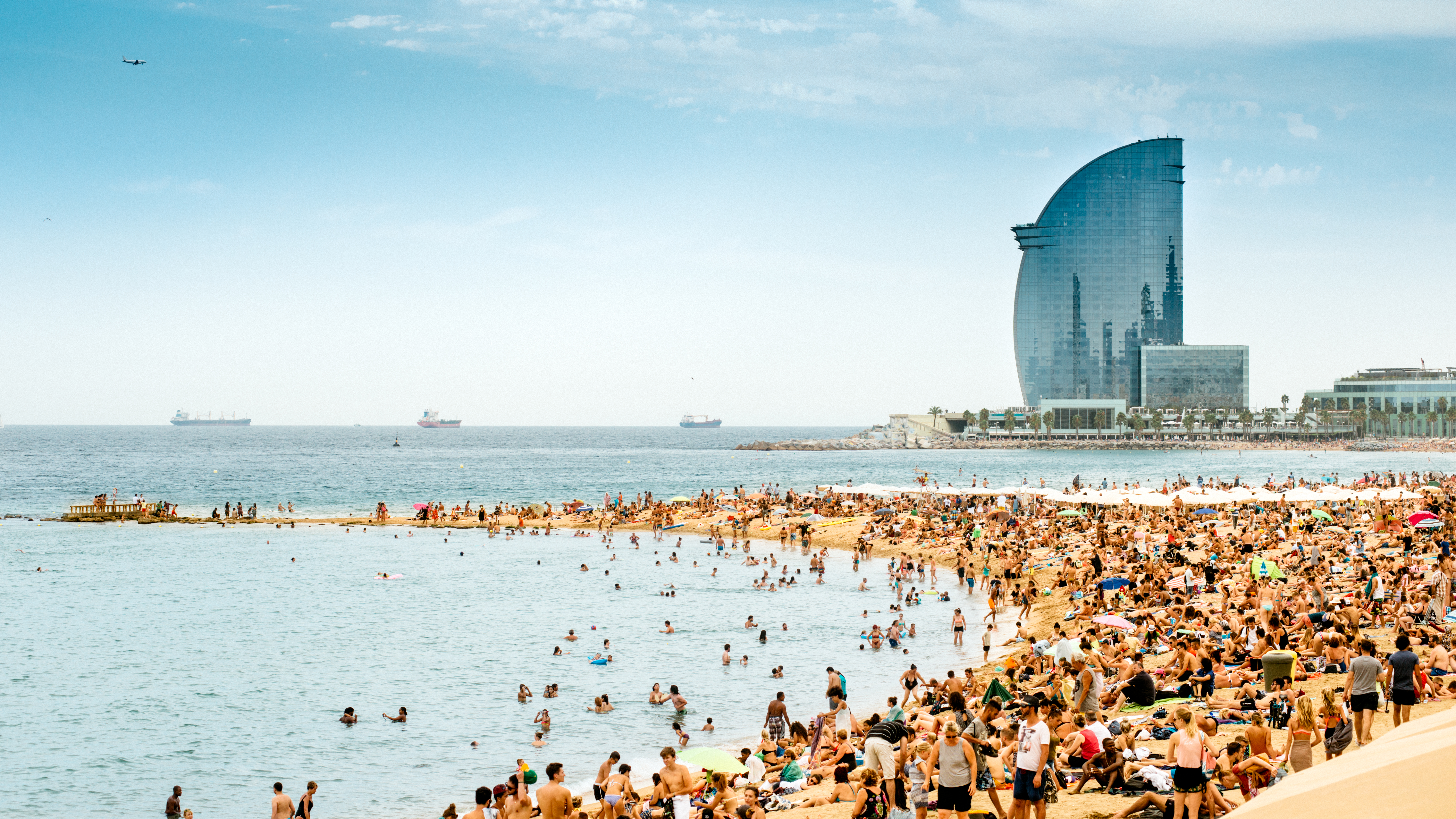 Bañistas en la concurrida playa de Barcelona, Hotel Vela y mar azul.