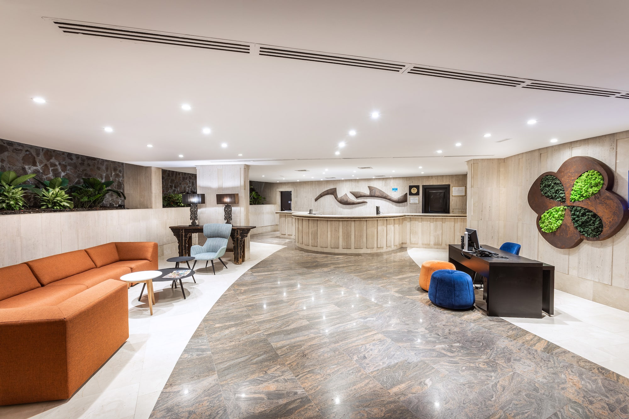 Modern hotel lobby reception with orange sofa, marble floors, and plant wall.