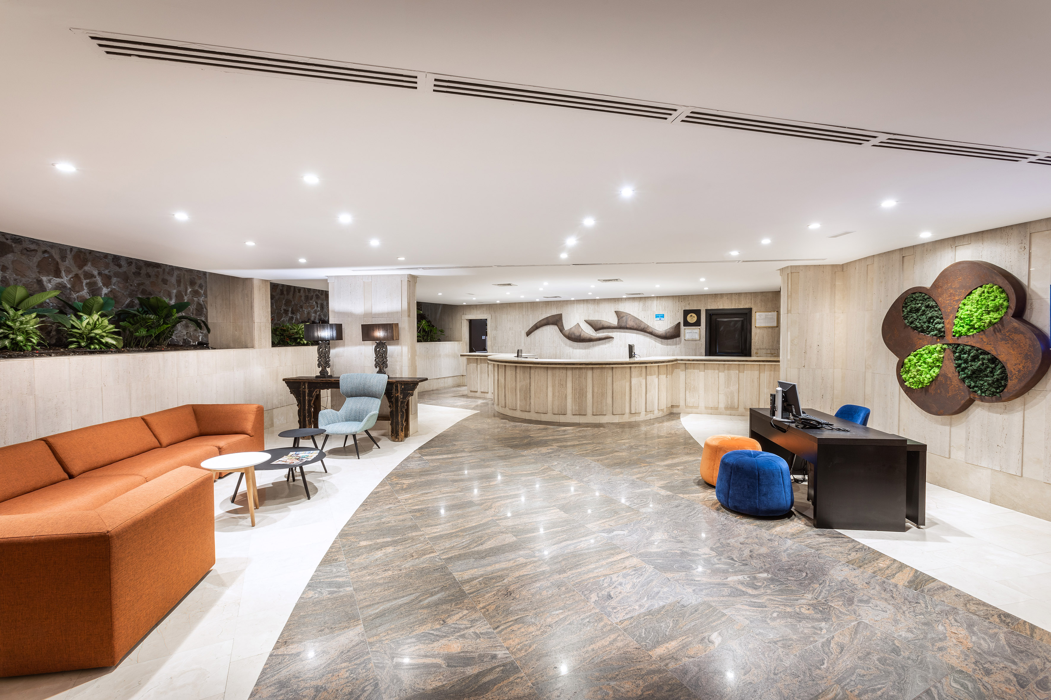 Modern hotel lobby reception with orange sofa, marble floors, and plant wall.