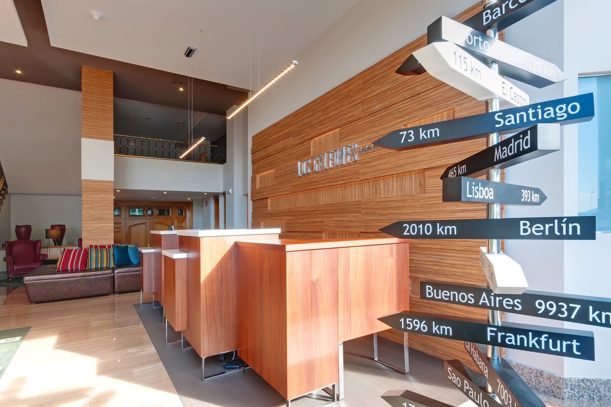 Modern hotel reception with wooden desk and directional signpost to global cities.