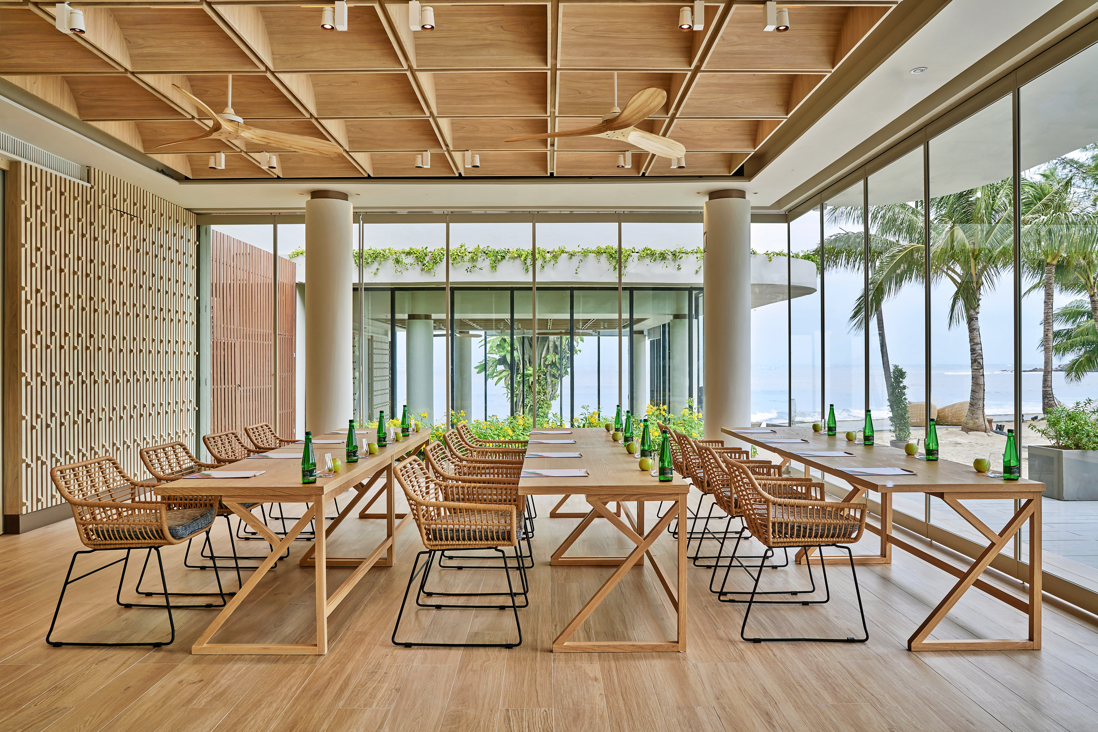 Modern conference room with ocean view, wooden tables, and rattan chairs.