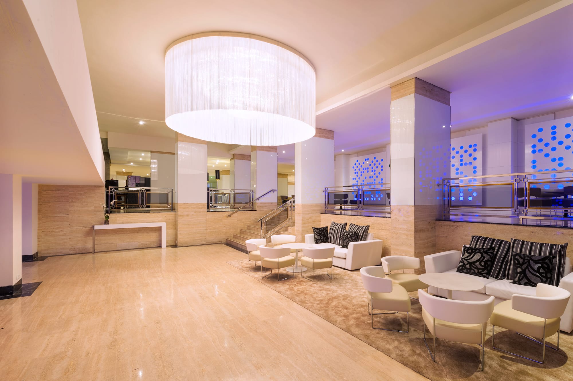 Modern hotel lobby with lounge seating, marble floors, and blue lighting.