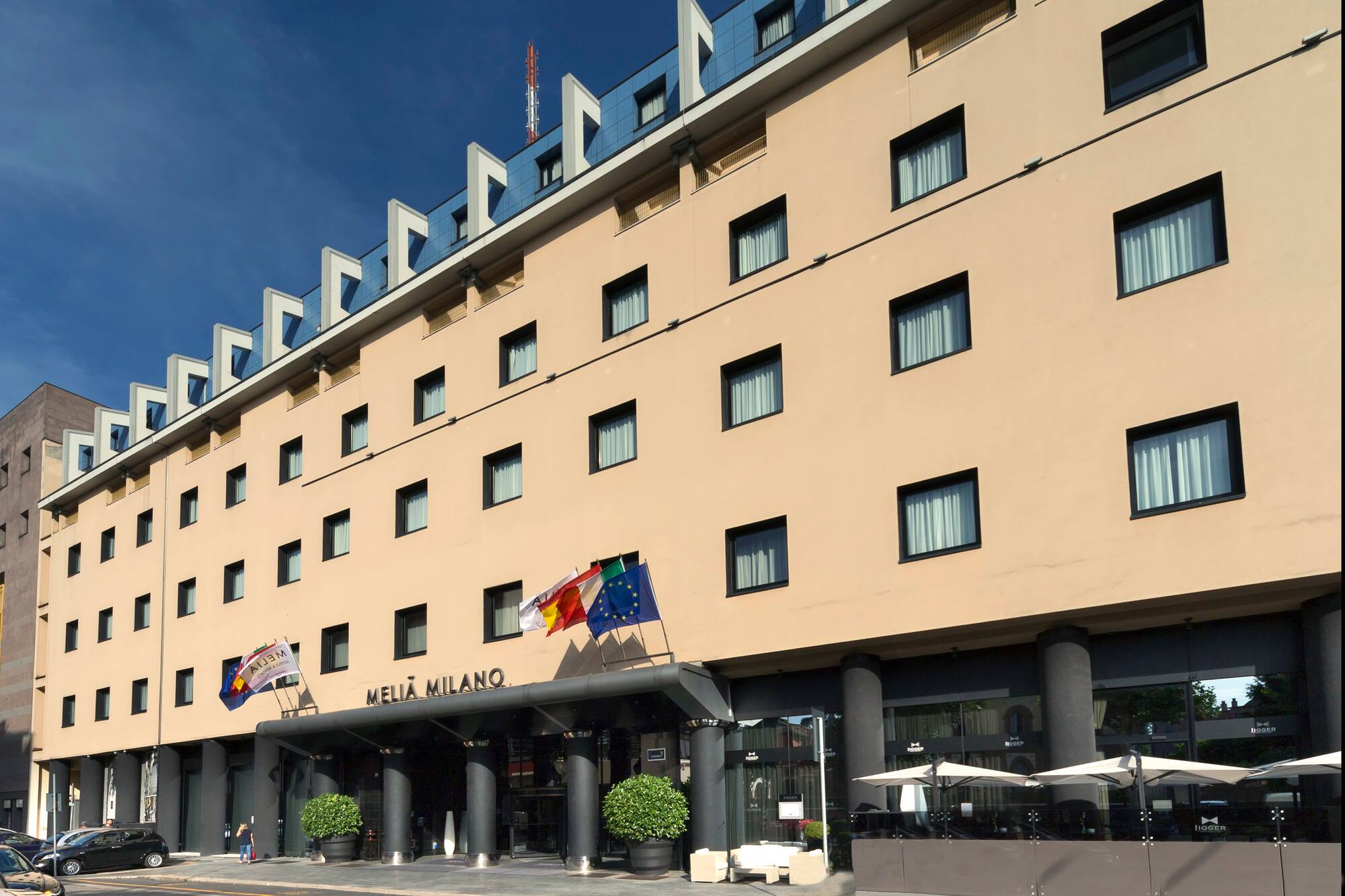 Meliá Milano hotel exterior in Milan, beige facade, modern blue roof, flags.