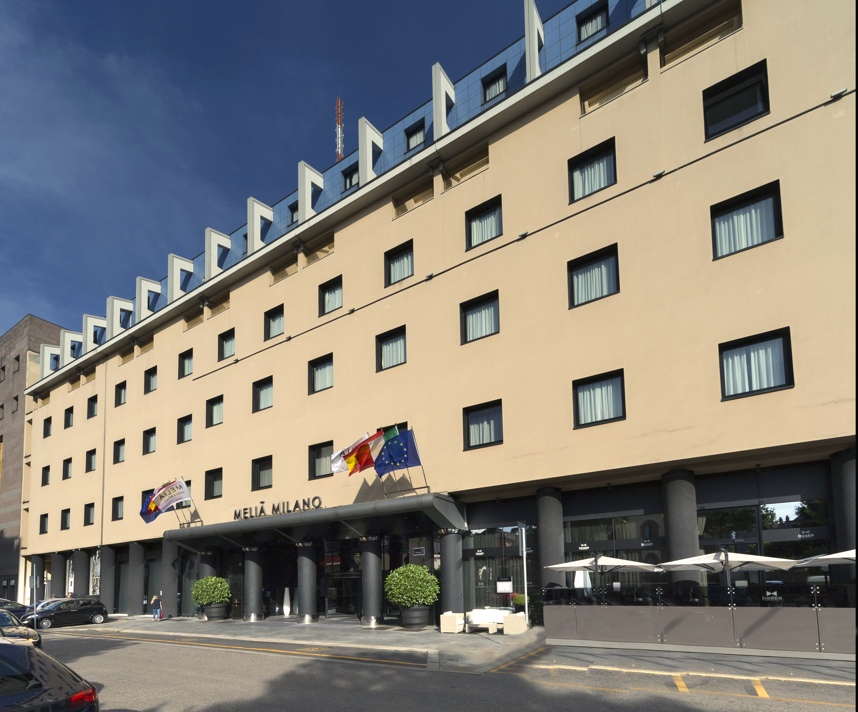 Meliá Milano hotel exterior in Milan, beige facade, modern blue roof, flags.